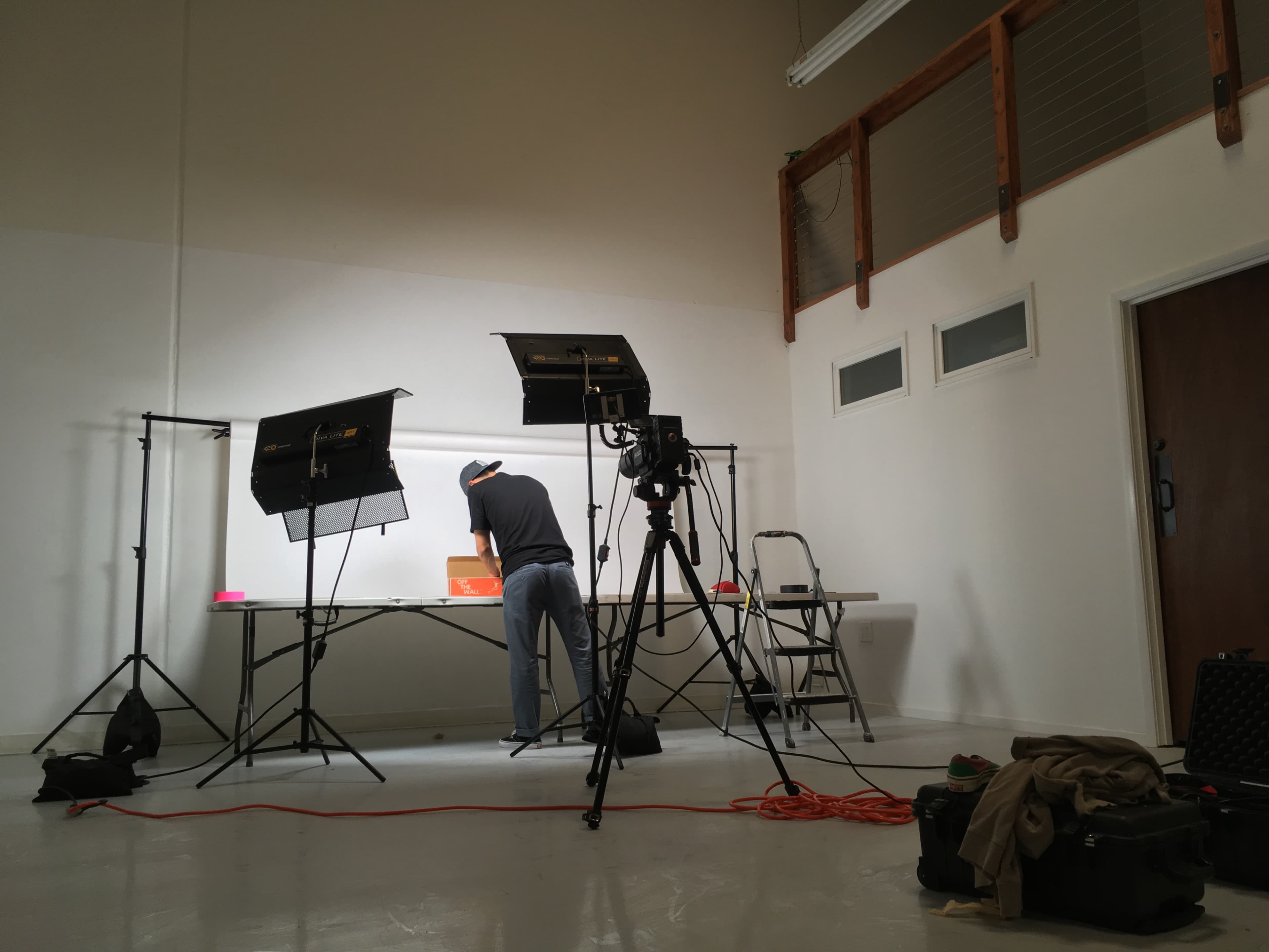 A photographer is setting up equipment in a spacious studio with bright lights and a backdrop for a photo shoot.