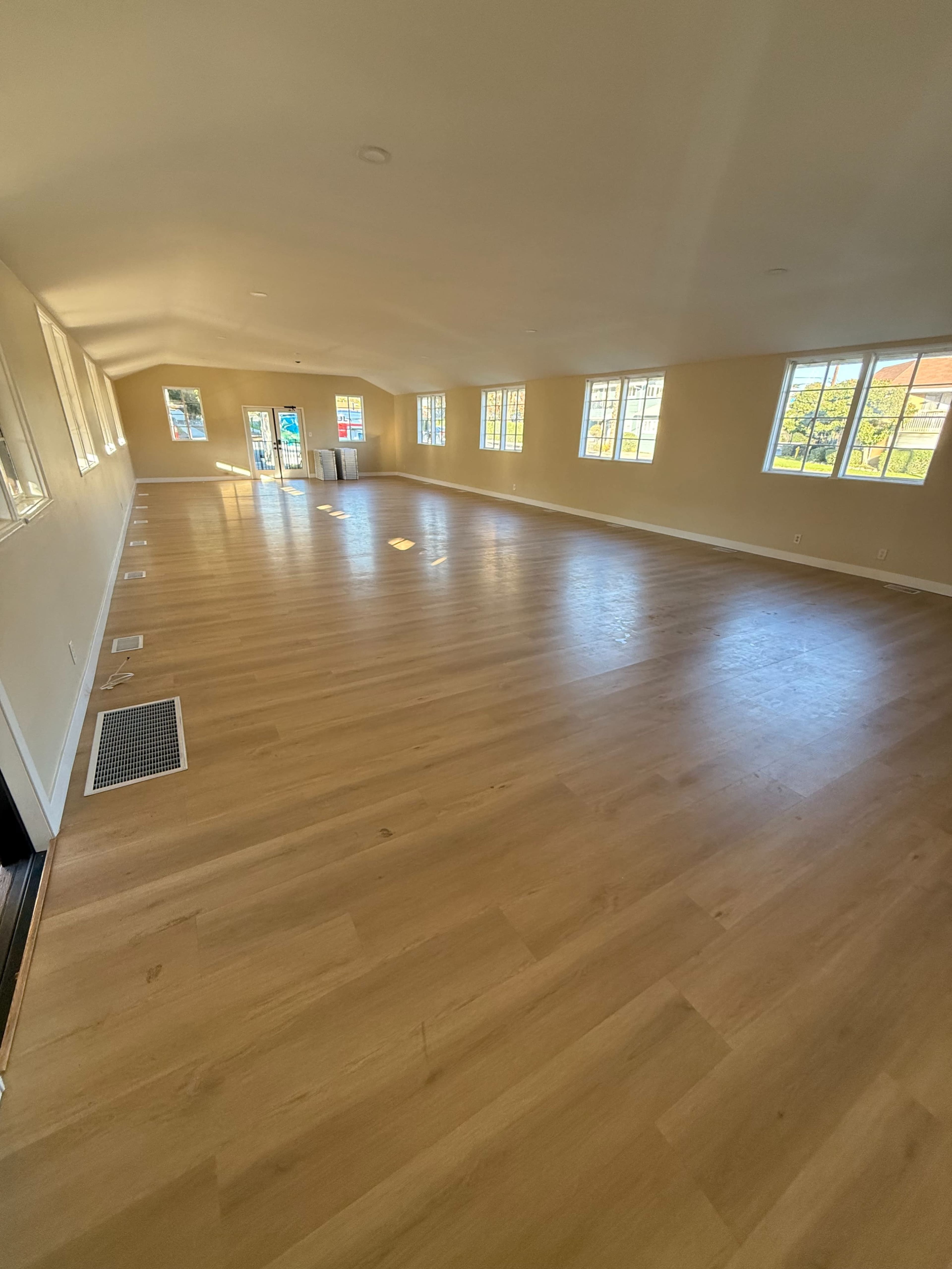 The image shows a spacious room with wooden flooring, large windows on either side, and a ceiling that slopes toward the center.