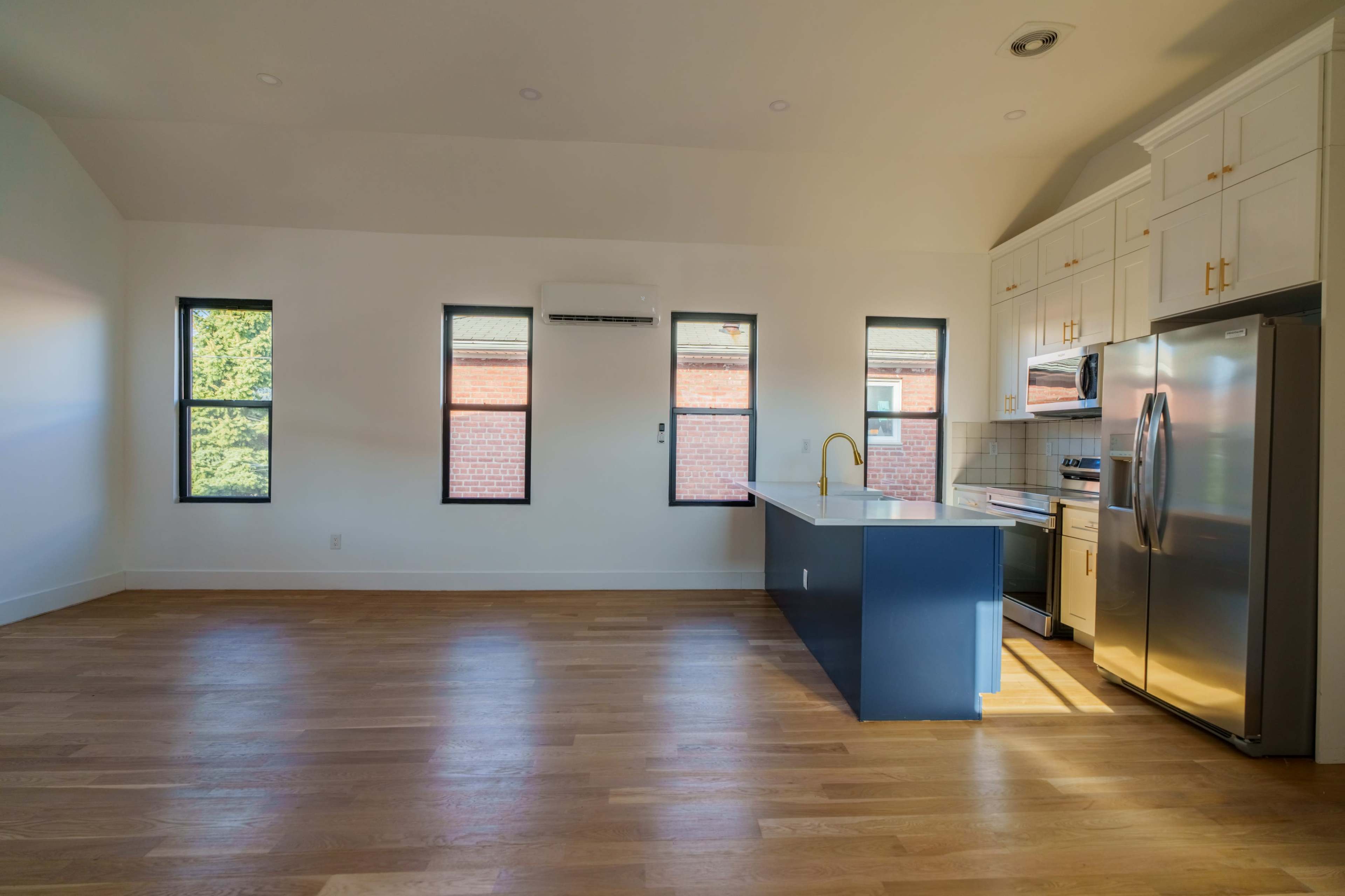 The image shows a bright, modern kitchen with a blue island, stainless steel appliances, and several large windows.
