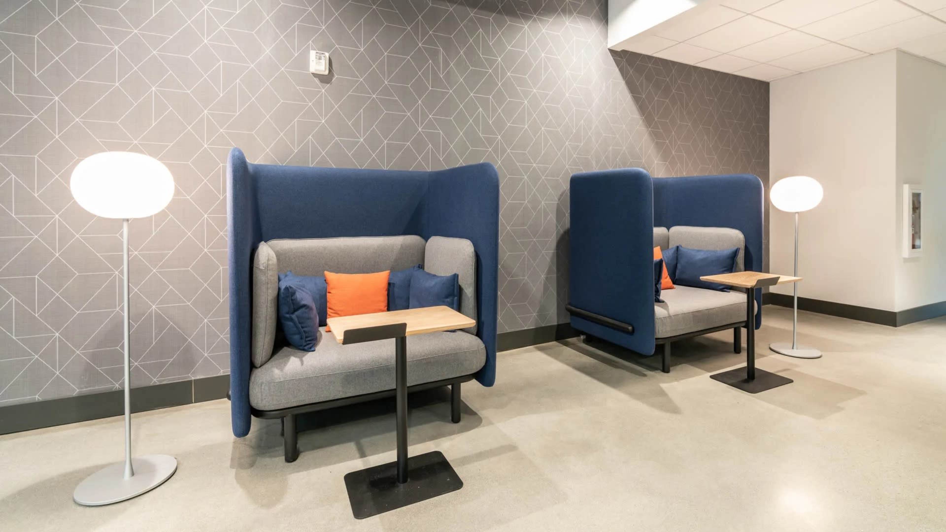 The image shows two modern seating areas with blue upholstered backrests and small tables against a decorative wall.