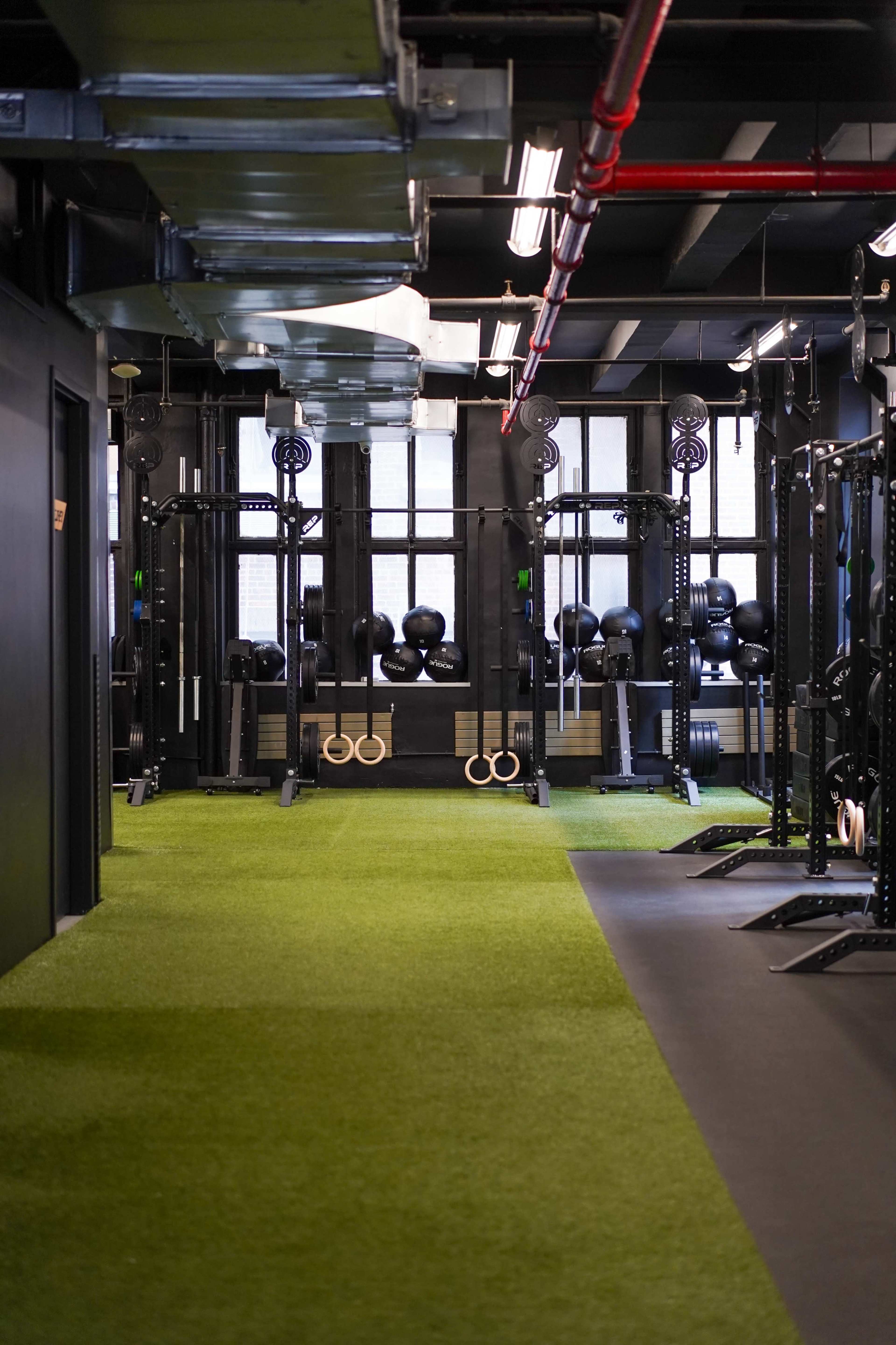 A gym with a turf floor, featuring weightlifting equipment and dumbbells arranged neatly along the walls.