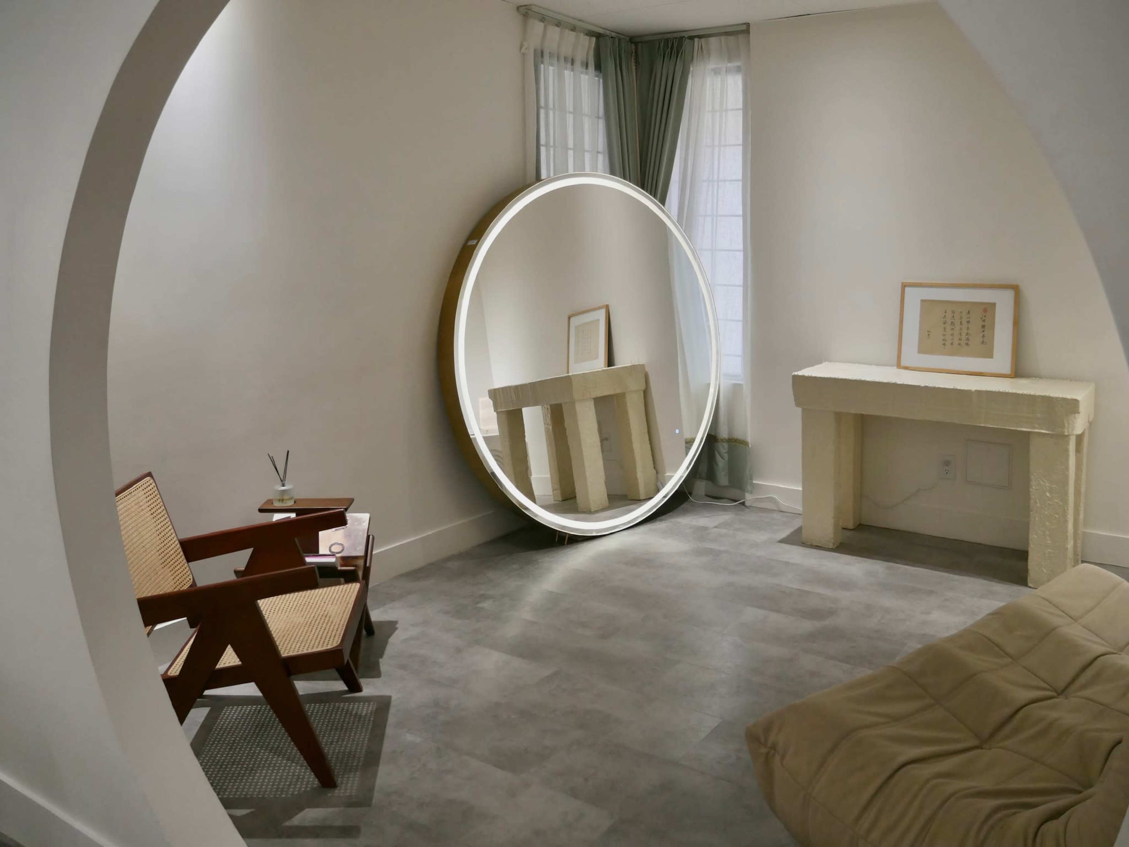 A minimalist room featuring a round mirror, a wooden chair, and a low stone-like console table.