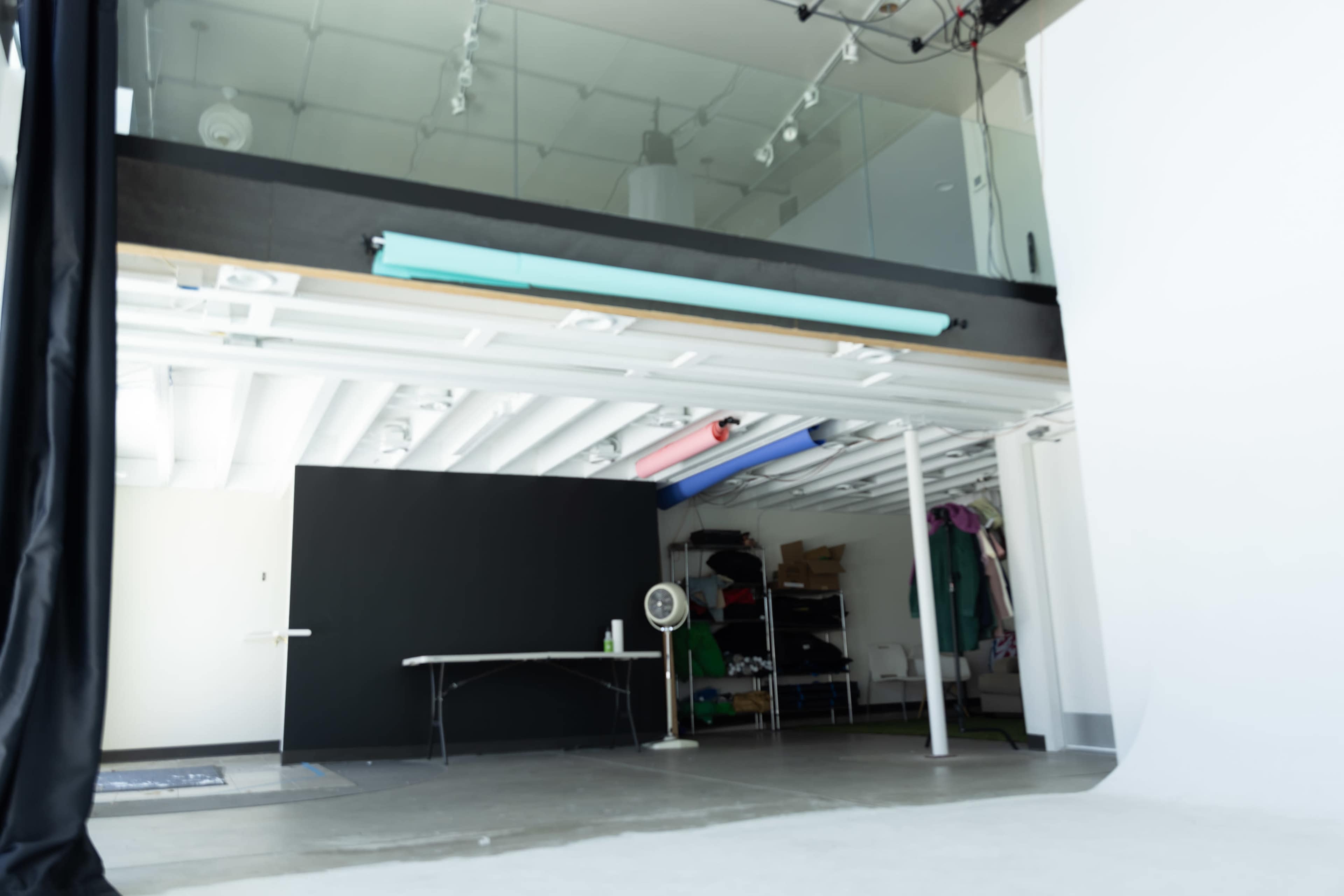 The image shows an open studio space with a black backdrop, a table, and various items stored on shelves in the background.