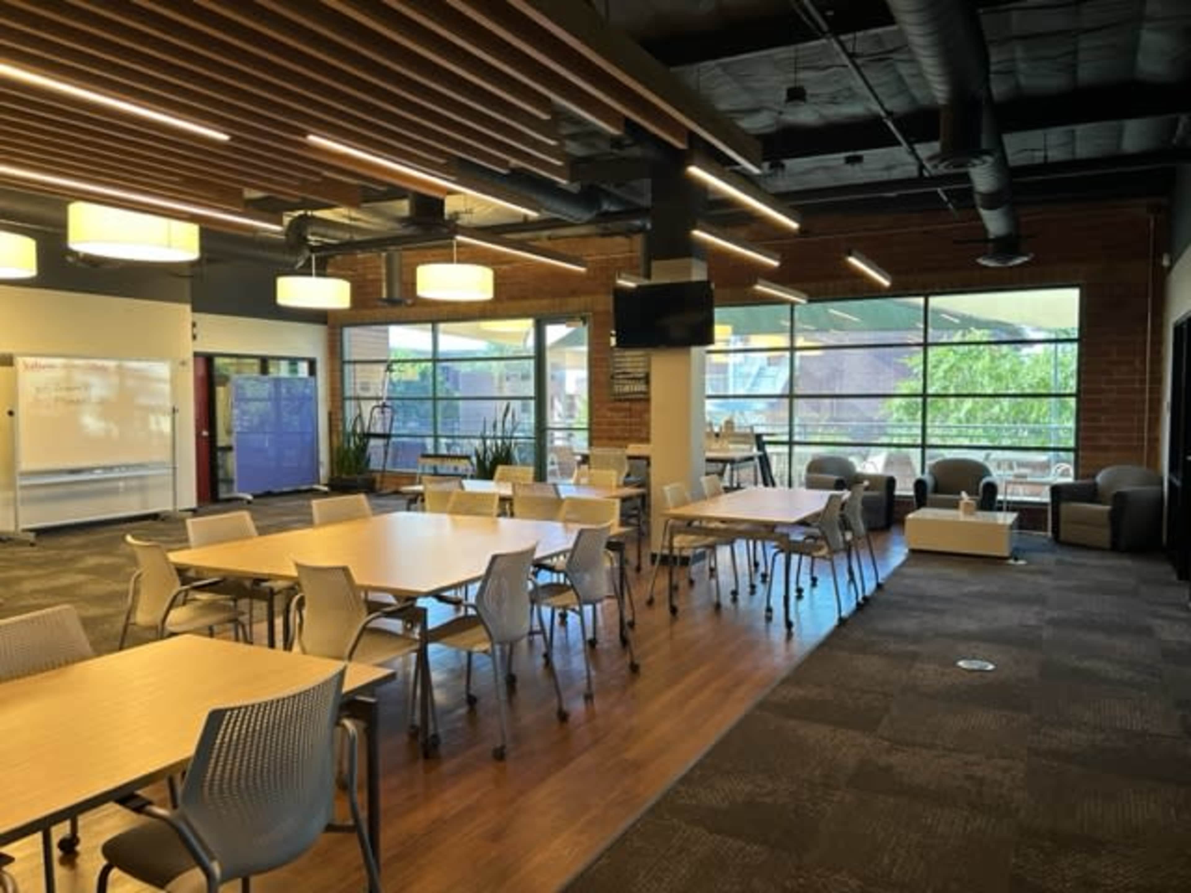 A modern office space featuring several tables and chairs, floor-to-ceiling windows, and various seating areas.