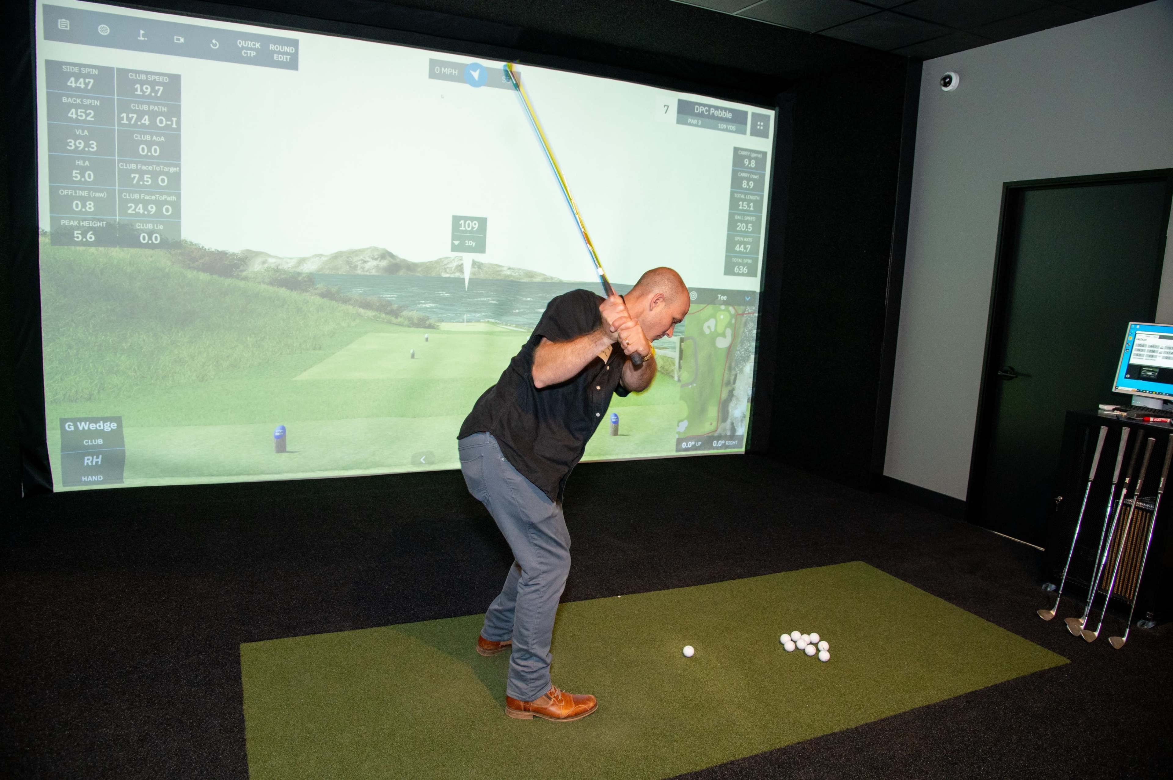 A man is swinging a golf club while preparing to hit a ball in an indoor golf simulator setup.