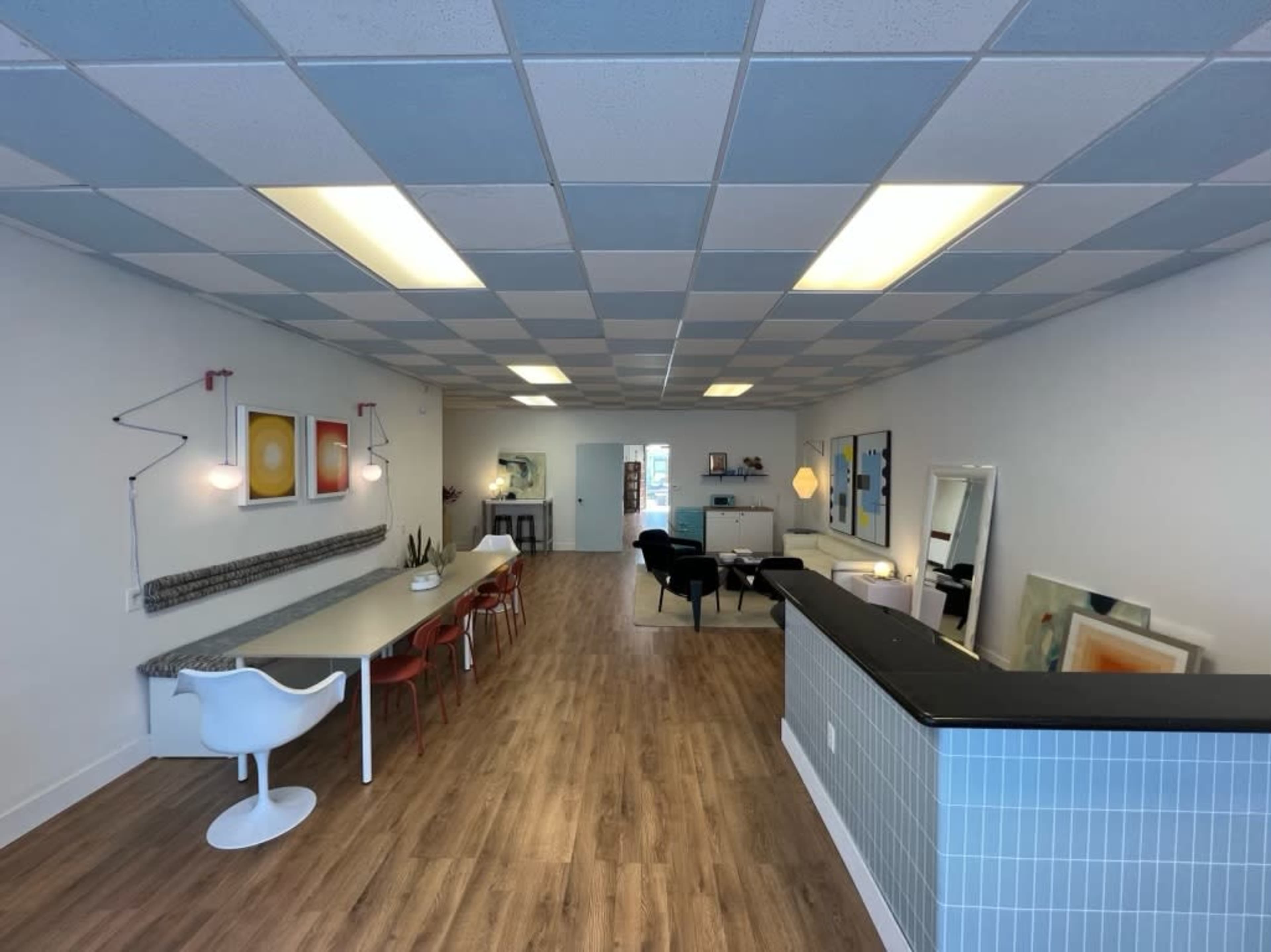 A modern, open interior space featuring a dining area with white chairs, a long table, and a reception desk in a minimalist design.