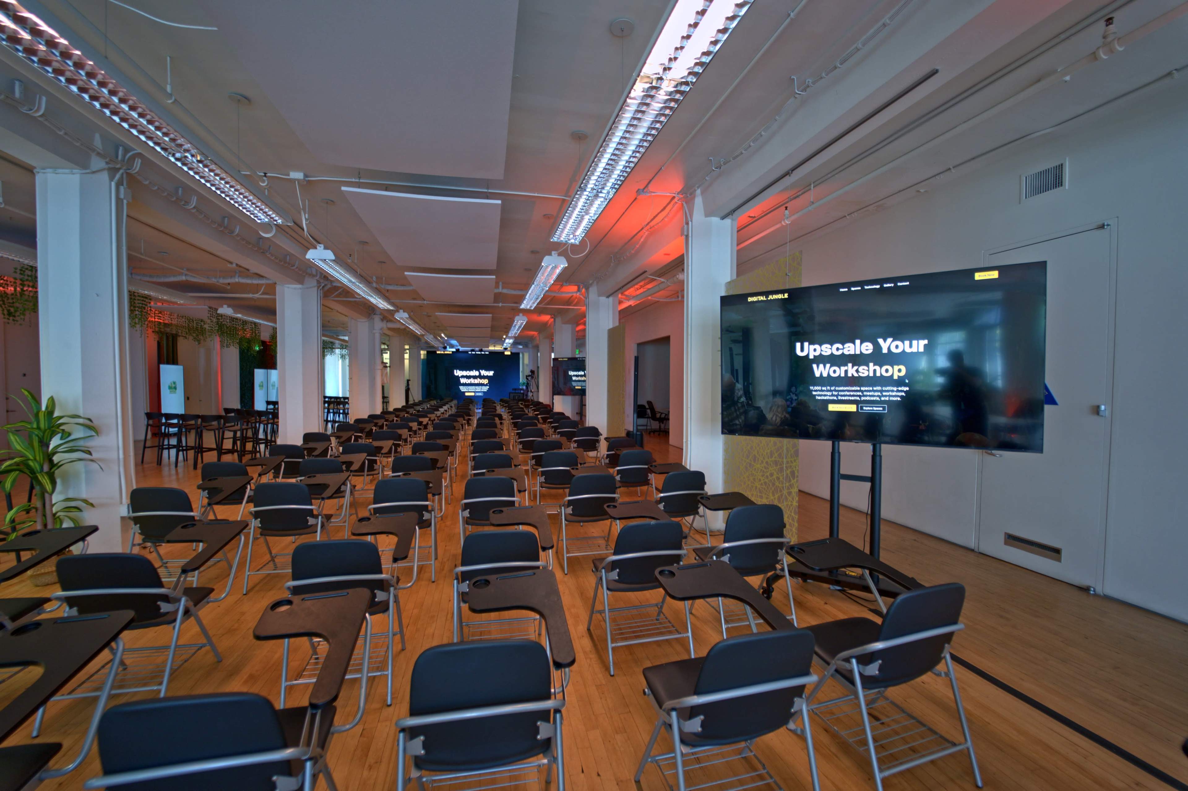 The image shows a spacious workshop venue with rows of empty black chairs facing large screens displaying "Upscale Your Workshop."