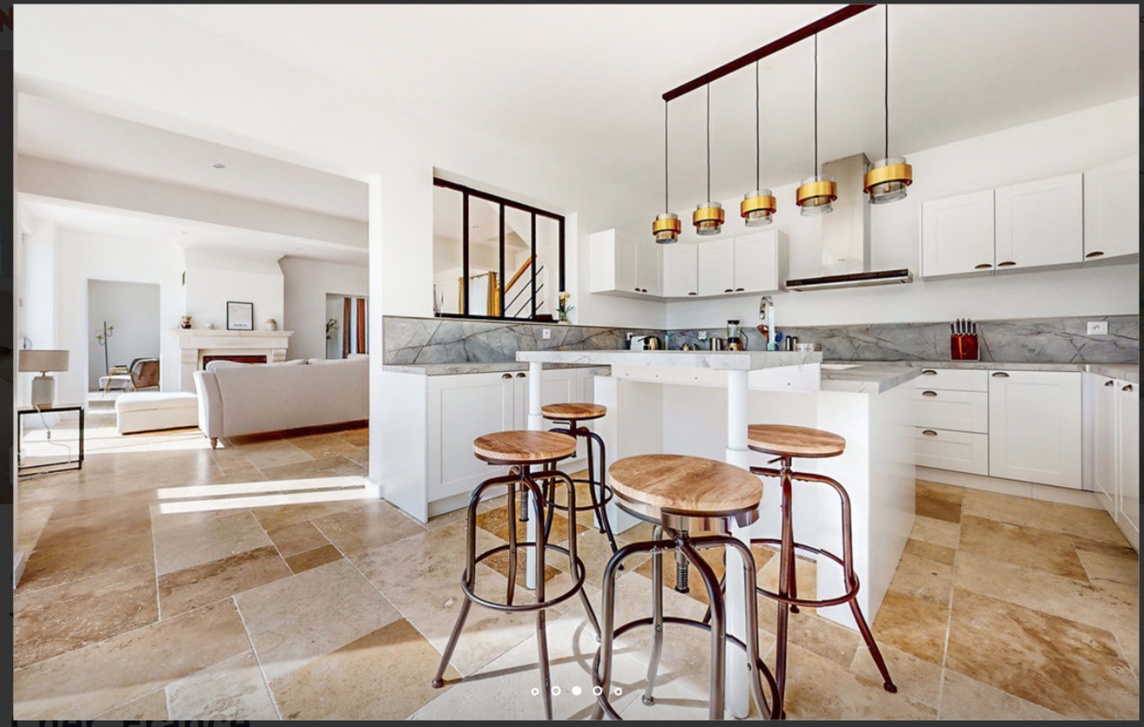 A modern kitchen features white cabinets, a central island with three wooden stools, and pendant lighting.