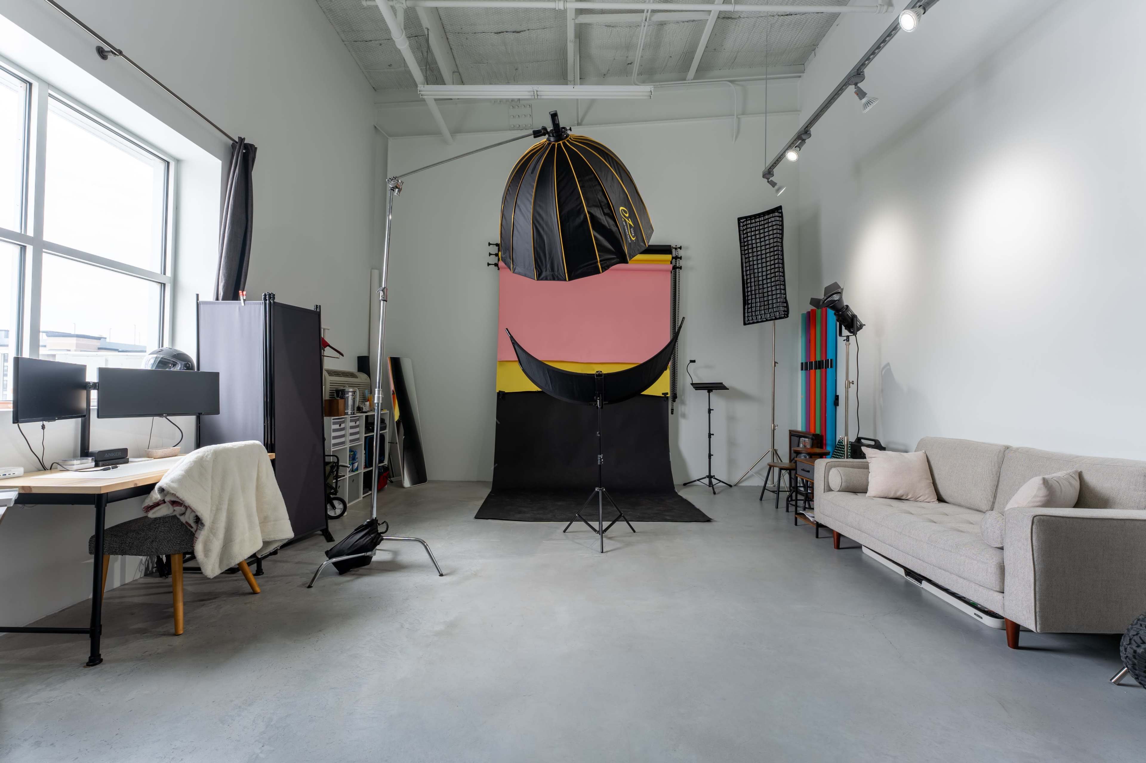 The image shows a photography studio with a large backdrop, photography equipment, and a seating area.