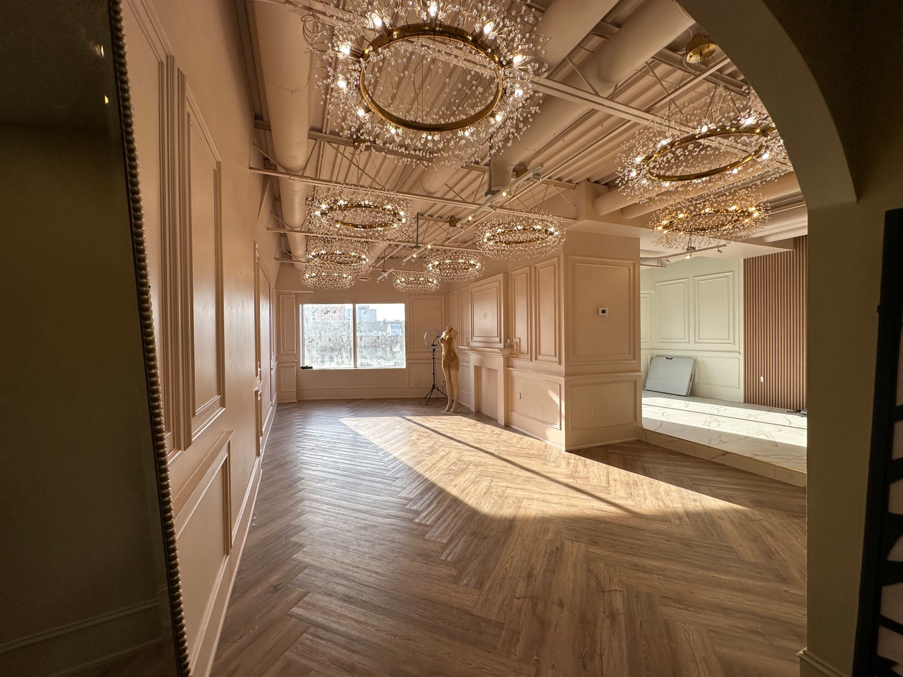 A spacious room with wooden herringbone flooring and multiple chandeliers hanging from the ceiling.
