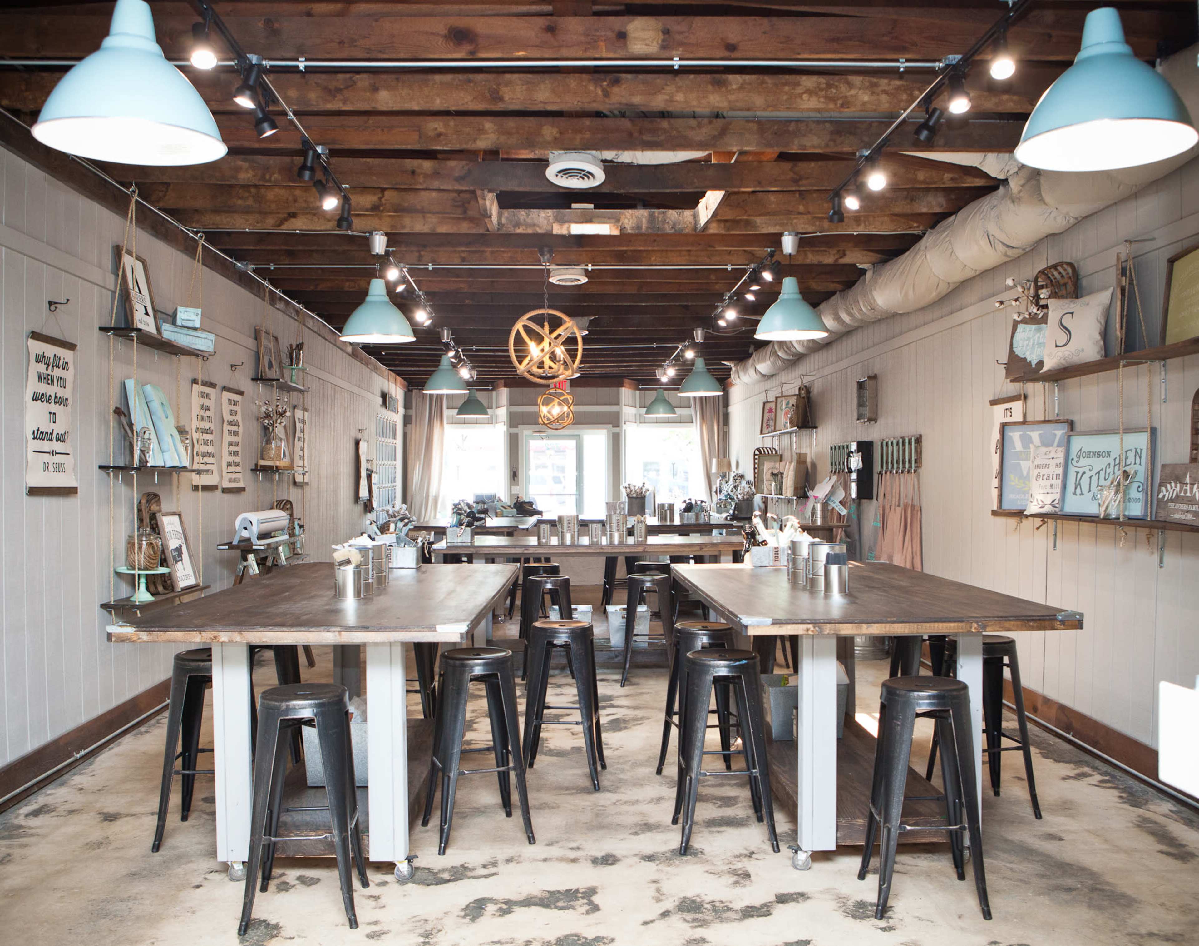 A spacious, well-lit interior of a kitchen workshop with wooden tables, metal stools, and various kitchen tools displayed on the walls.