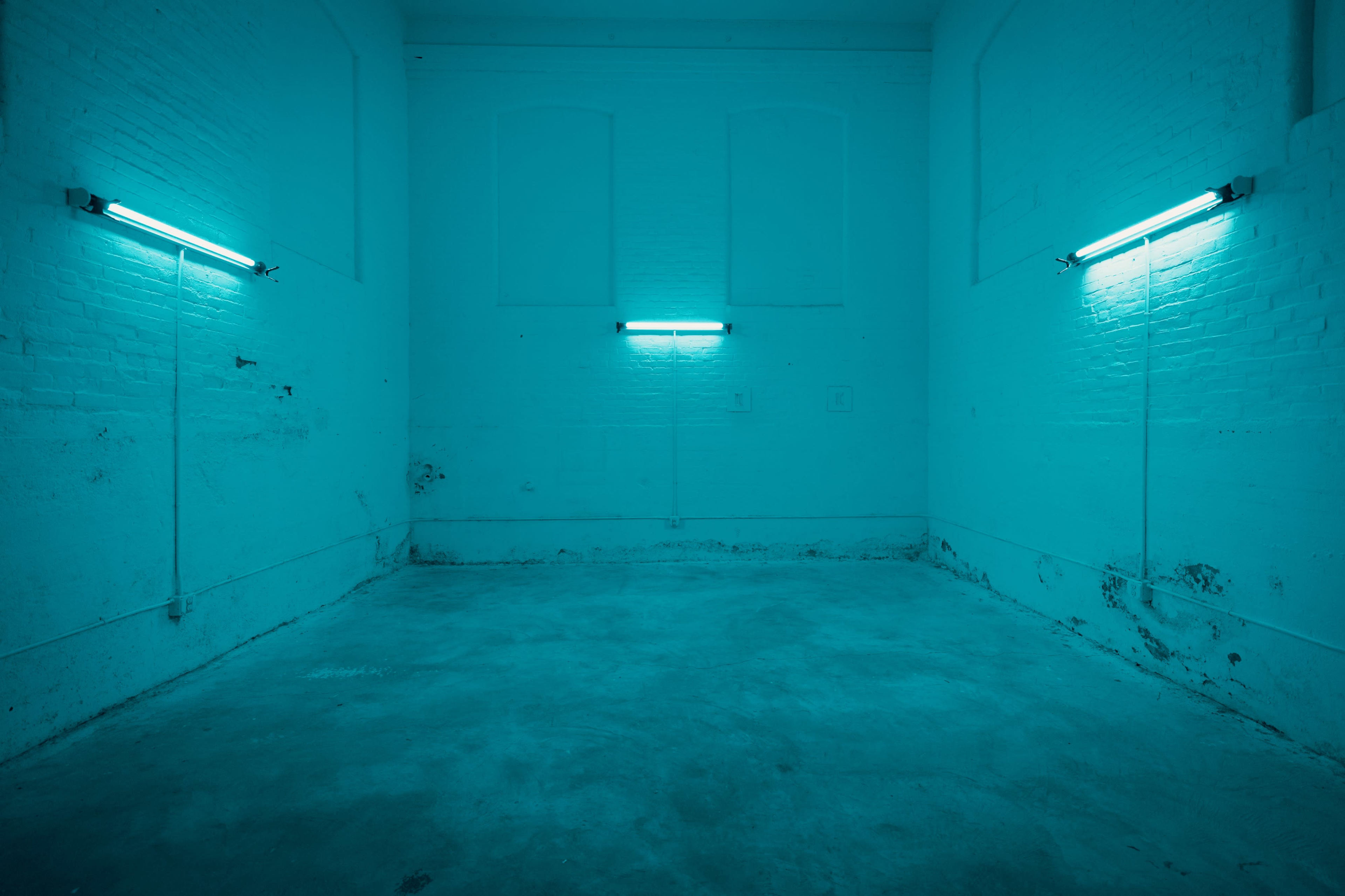 An empty room with turquoise walls and two fluorescent light fixtures mounted on the walls.