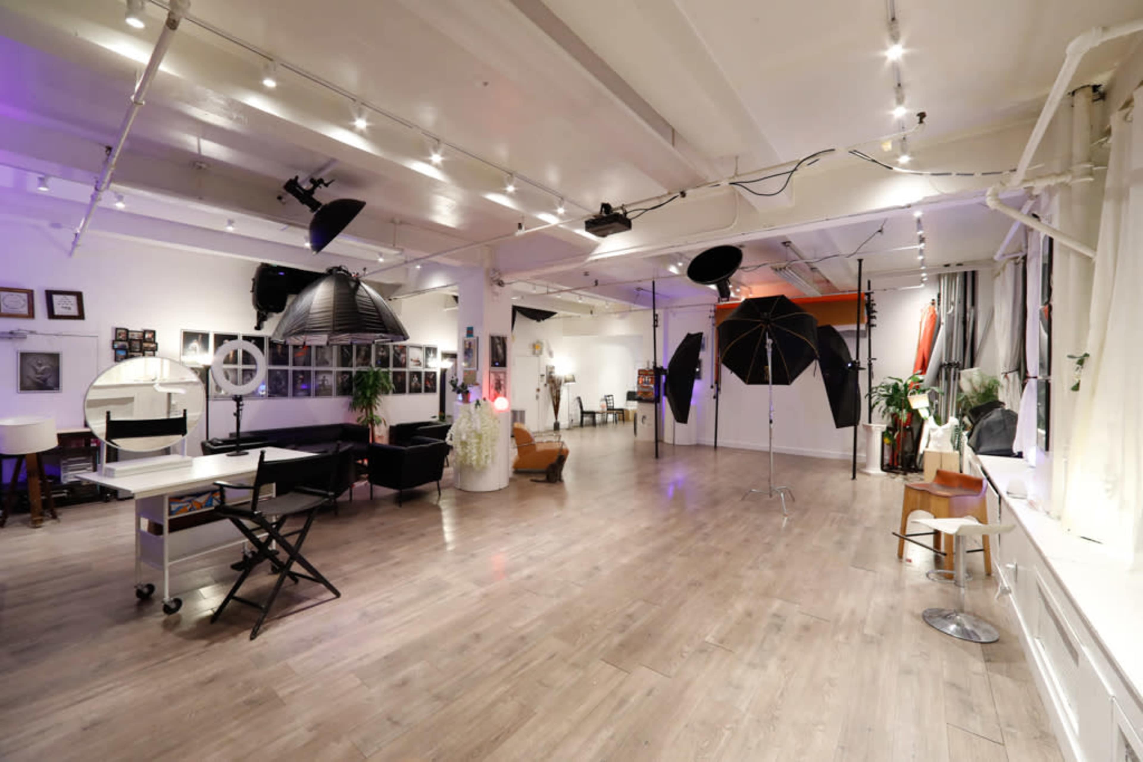 A spacious photography studio is equipped with lighting equipment, a seating area, and various props along the walls.