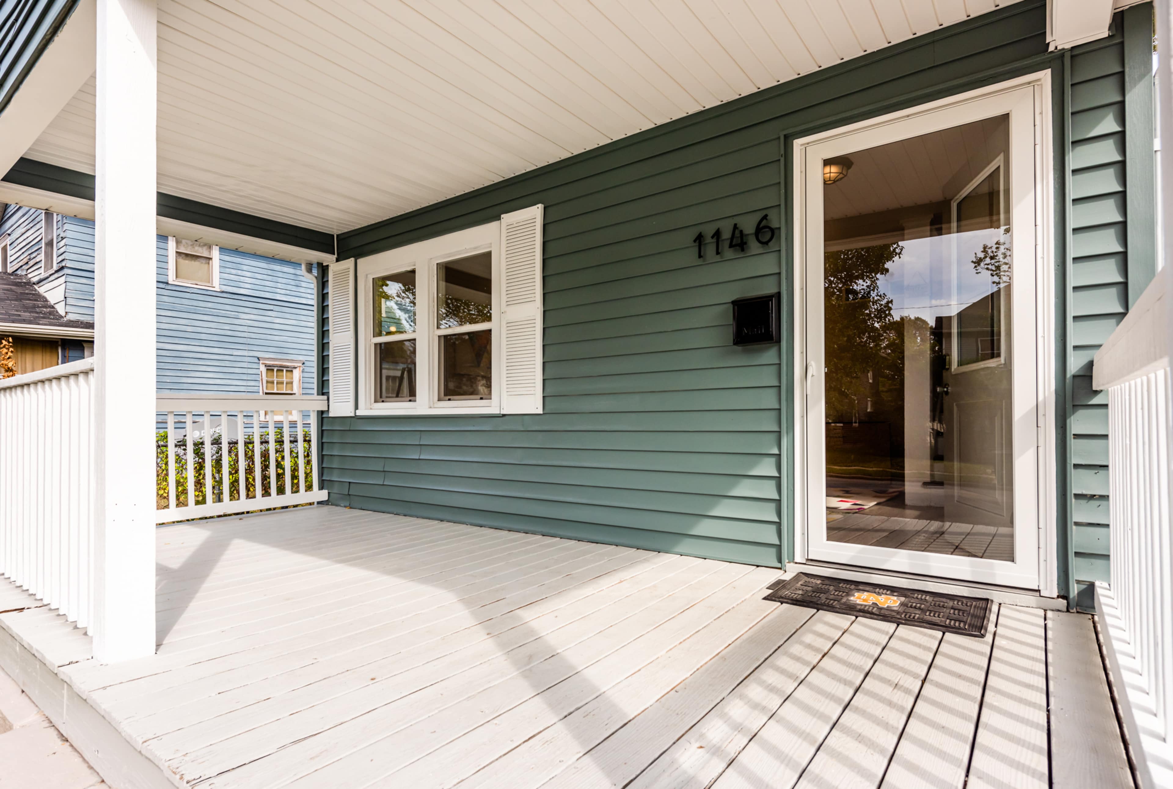 A green house with a covered porch and a front door featuring a large window beside it.
