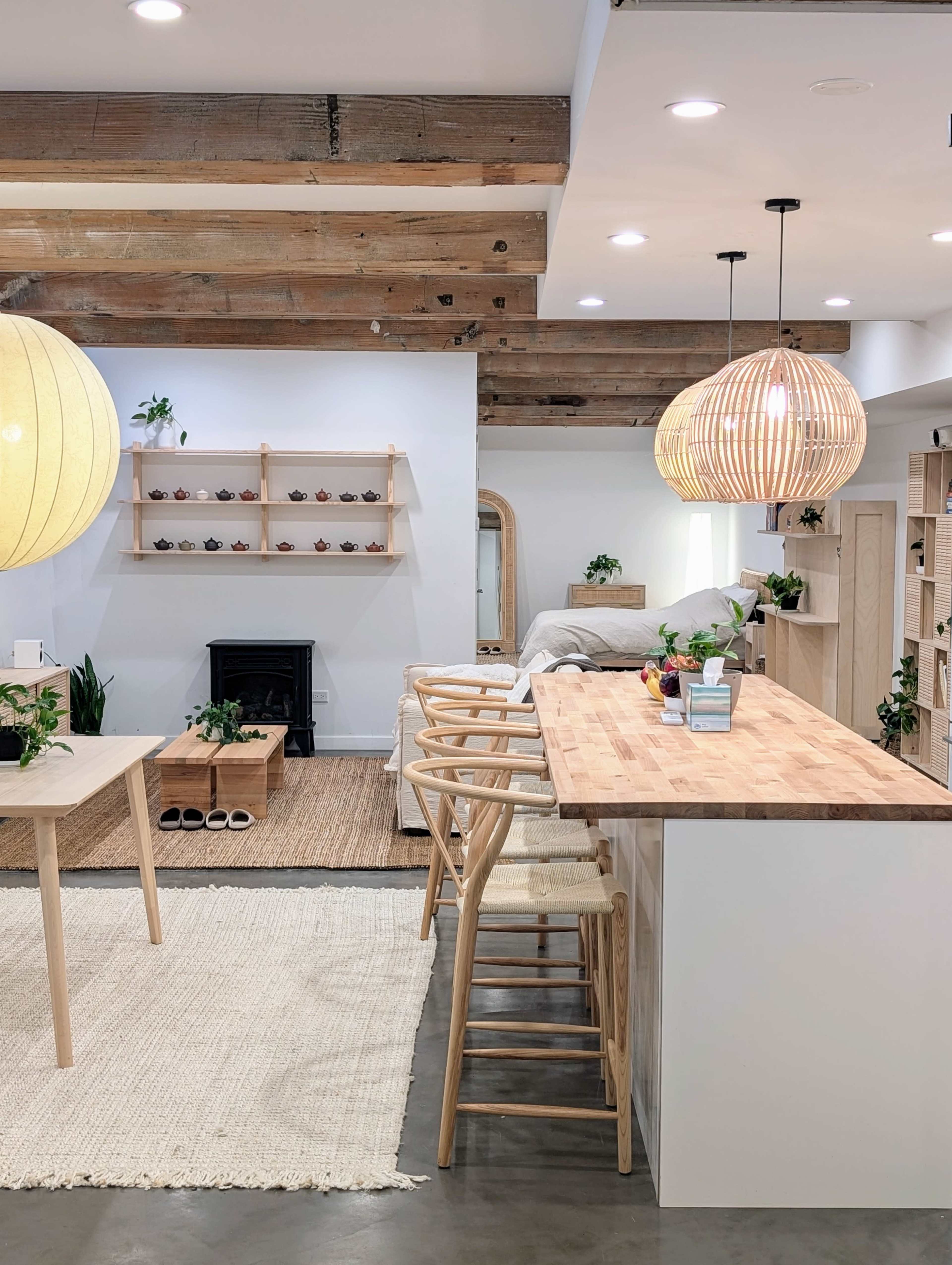 A modern living space with wooden beams, a light-colored kitchen island, bar stools, and various plants arranged throughout.