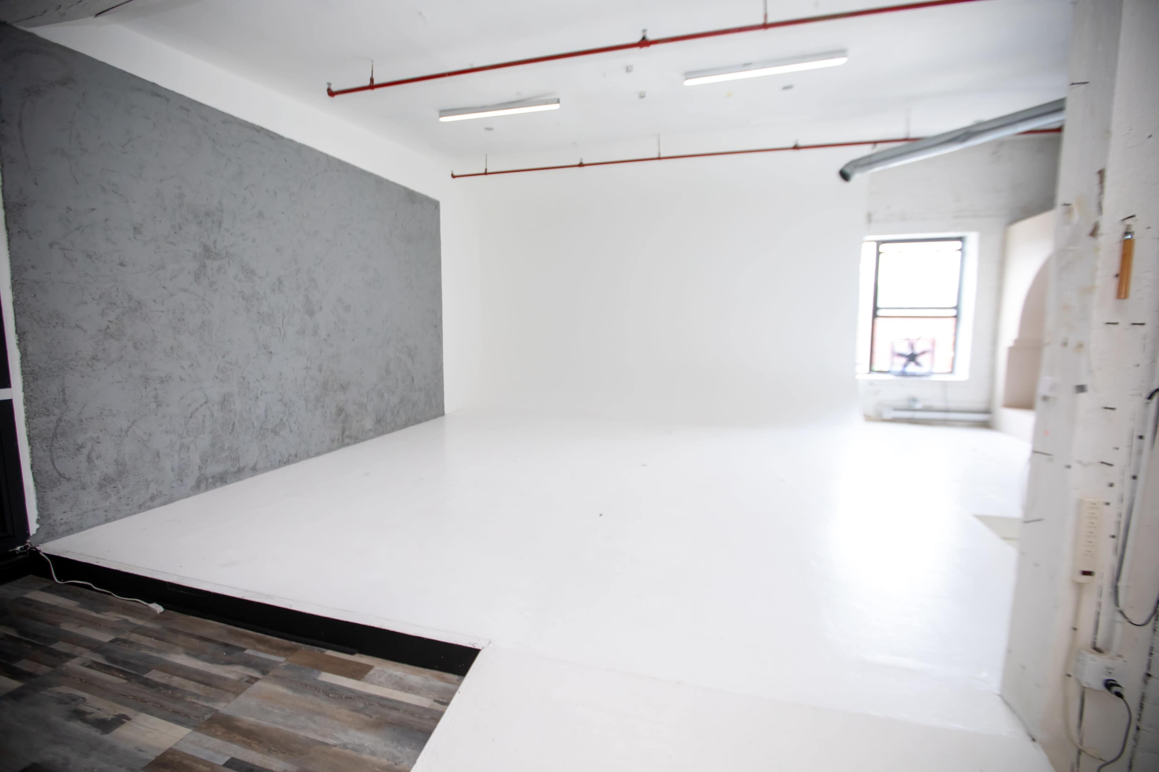 The image shows a spacious photography studio with a large white floor and one gray wall.