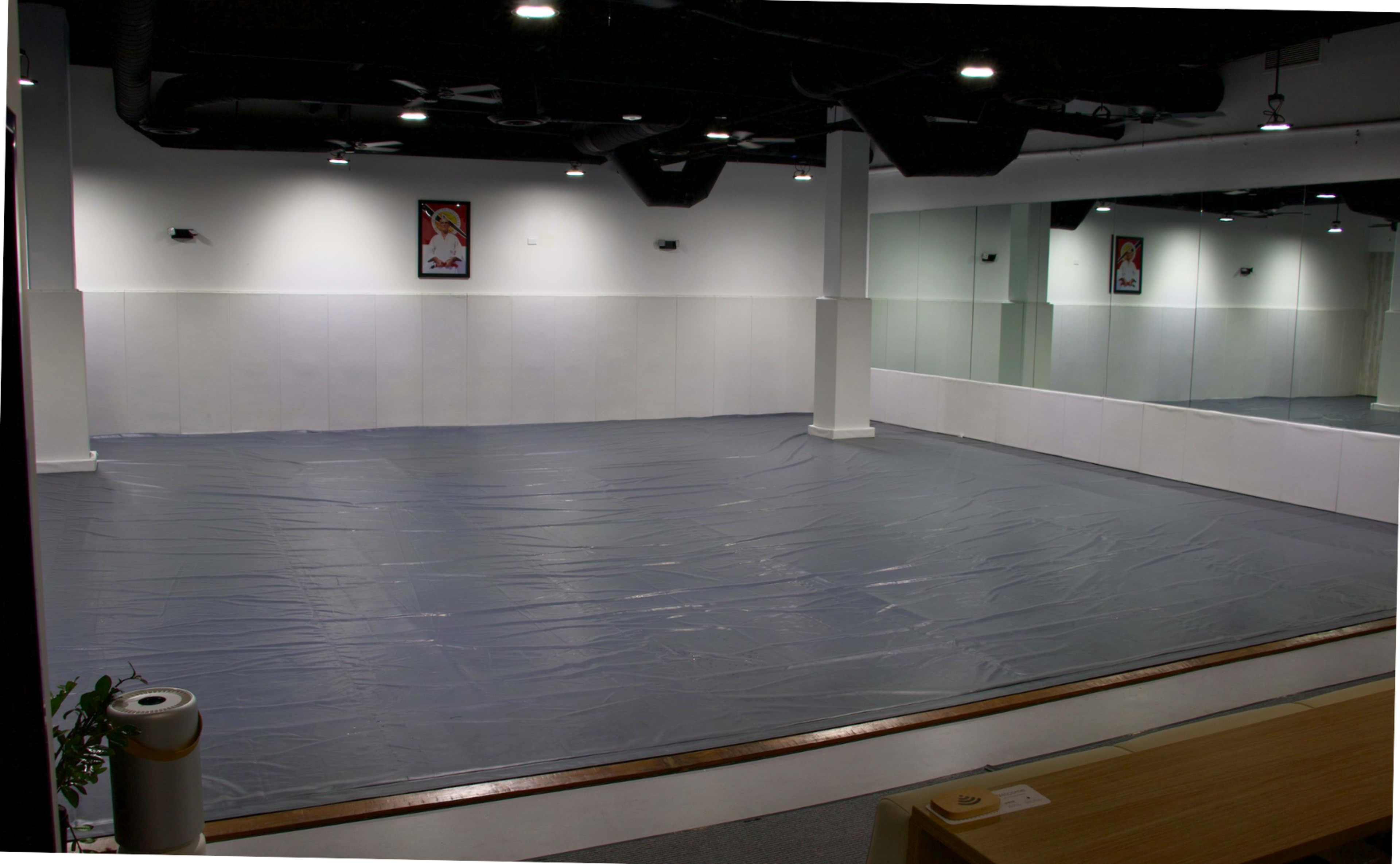 The image shows a spacious, empty room with a gray tarp covering the floor and large mirrors on one wall.