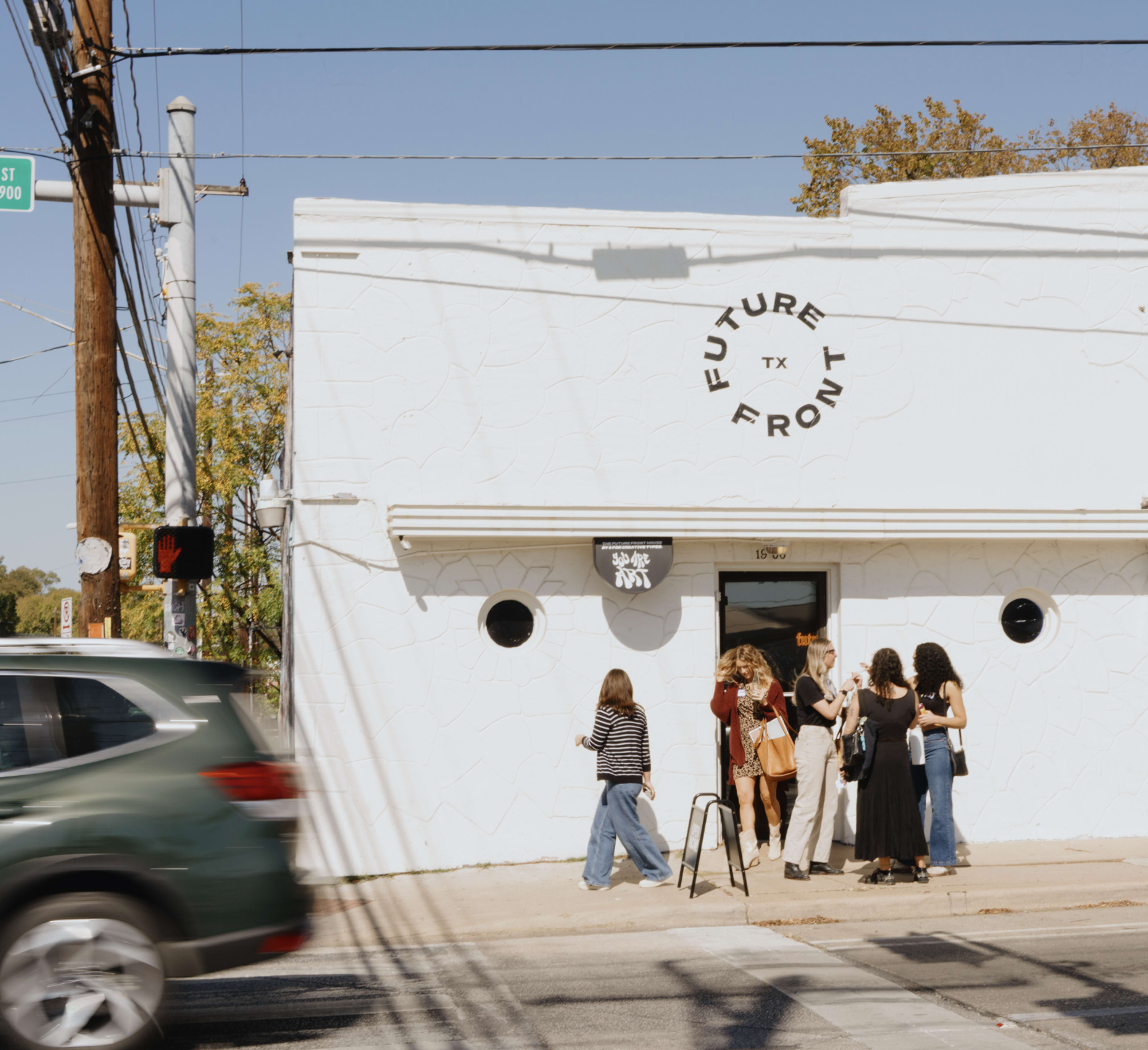 A group of people stands outside a white building with the sign "FUTURE TX" on a sunny day.