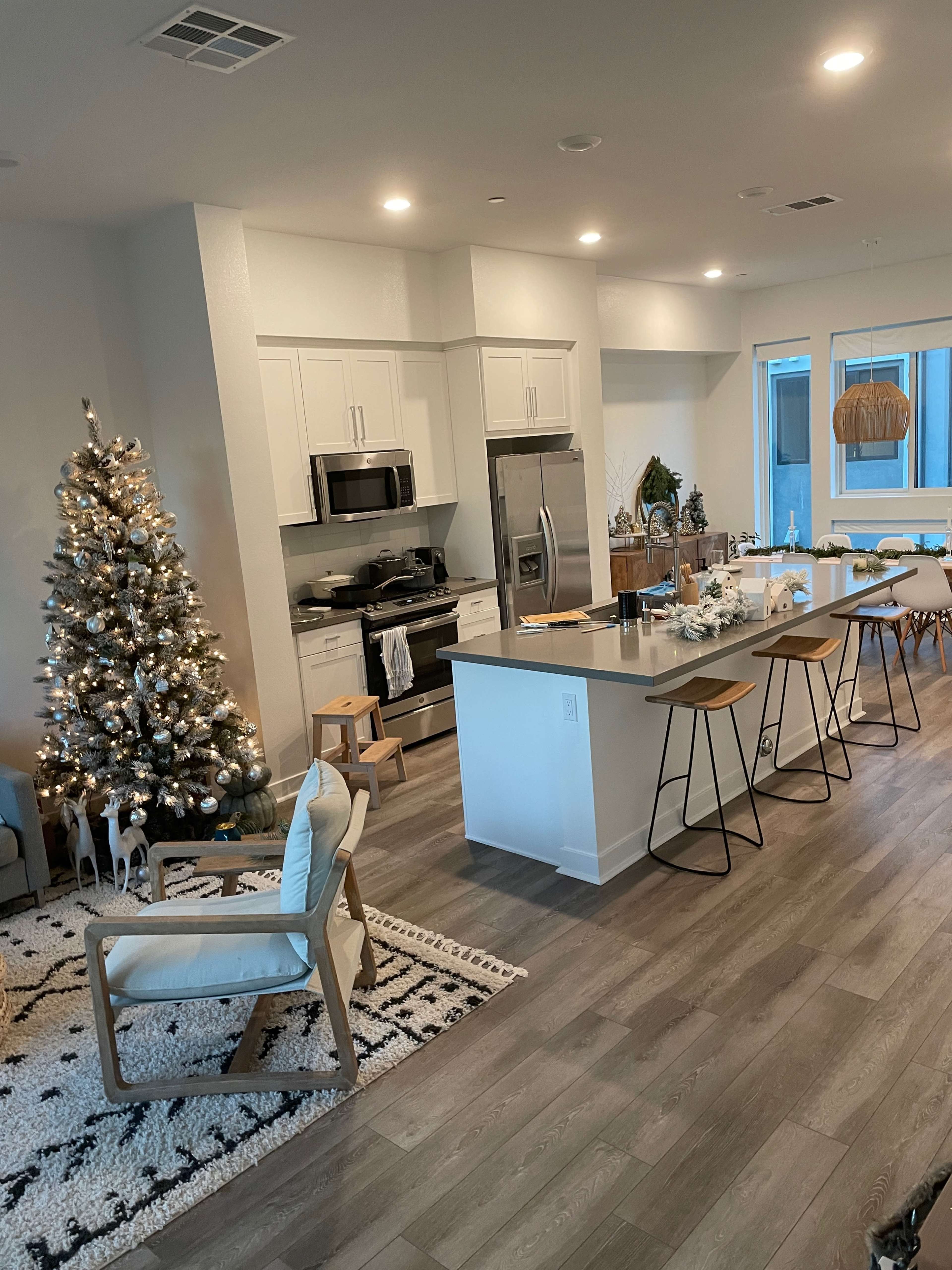 A modern kitchen and dining area decorated for the holidays, featuring a Christmas tree, a dining table, and bar stools.