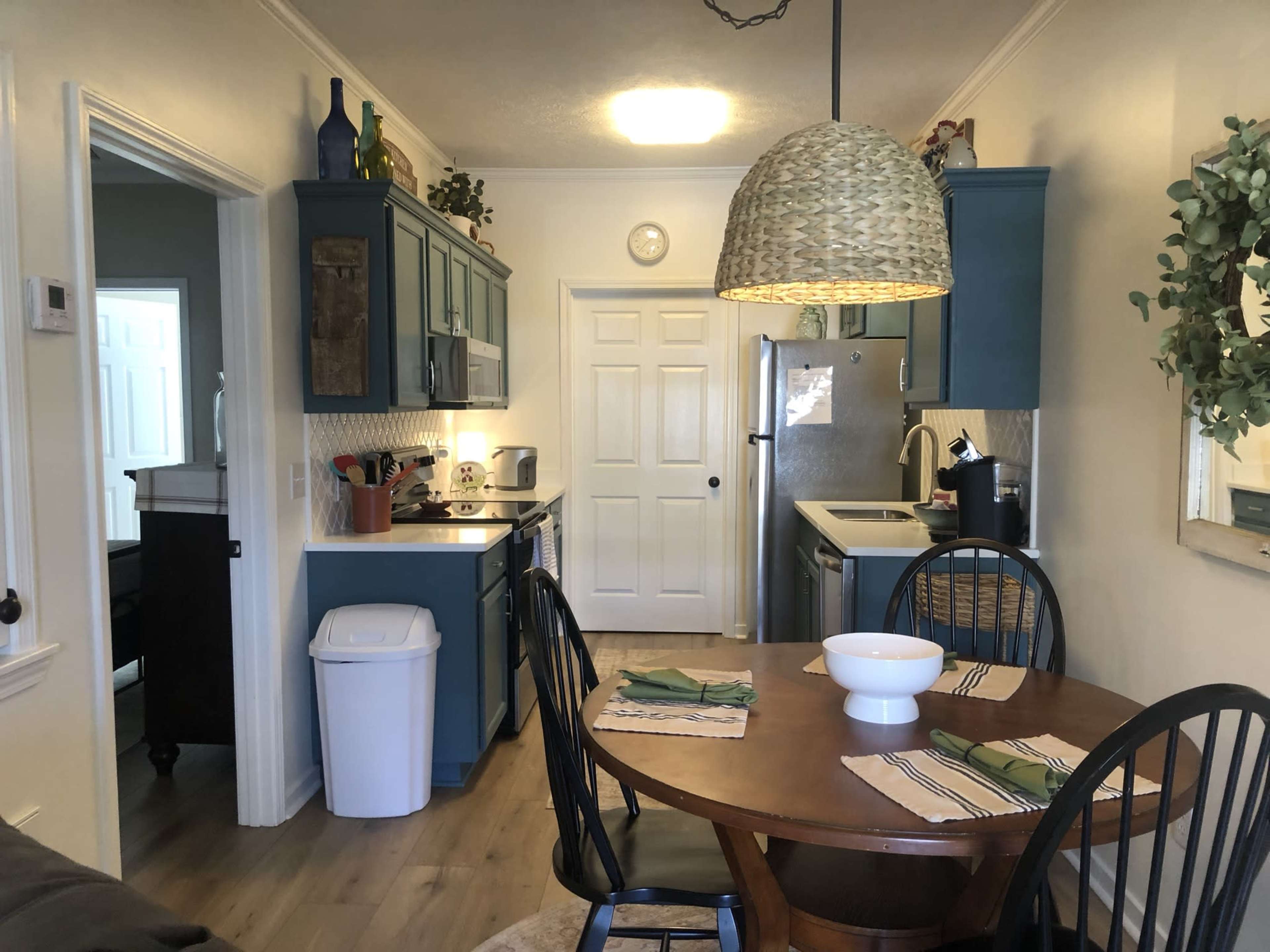 A kitchen and dining area featuring blue cabinets, a round wooden table set for a meal, and an open door leading to another room.