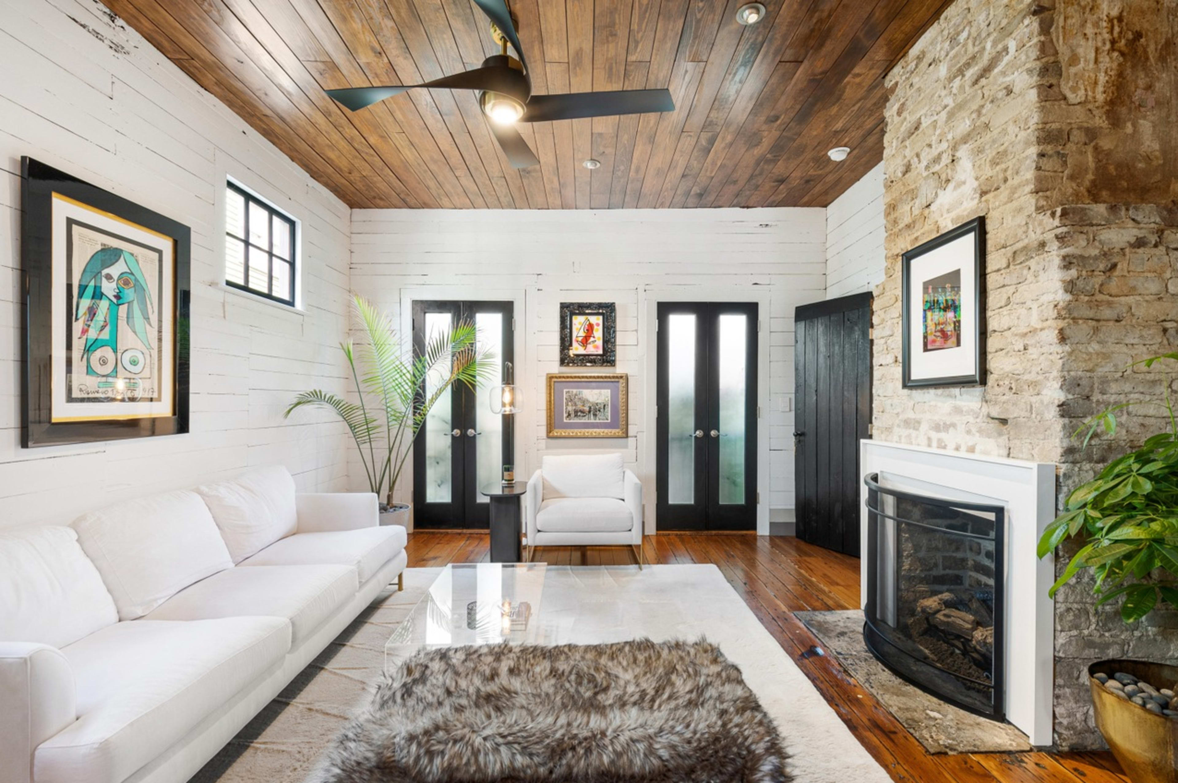 The living room features a white sofa, a stone fireplace, and large windows set against a backdrop of rustic wooden walls and ceiling.