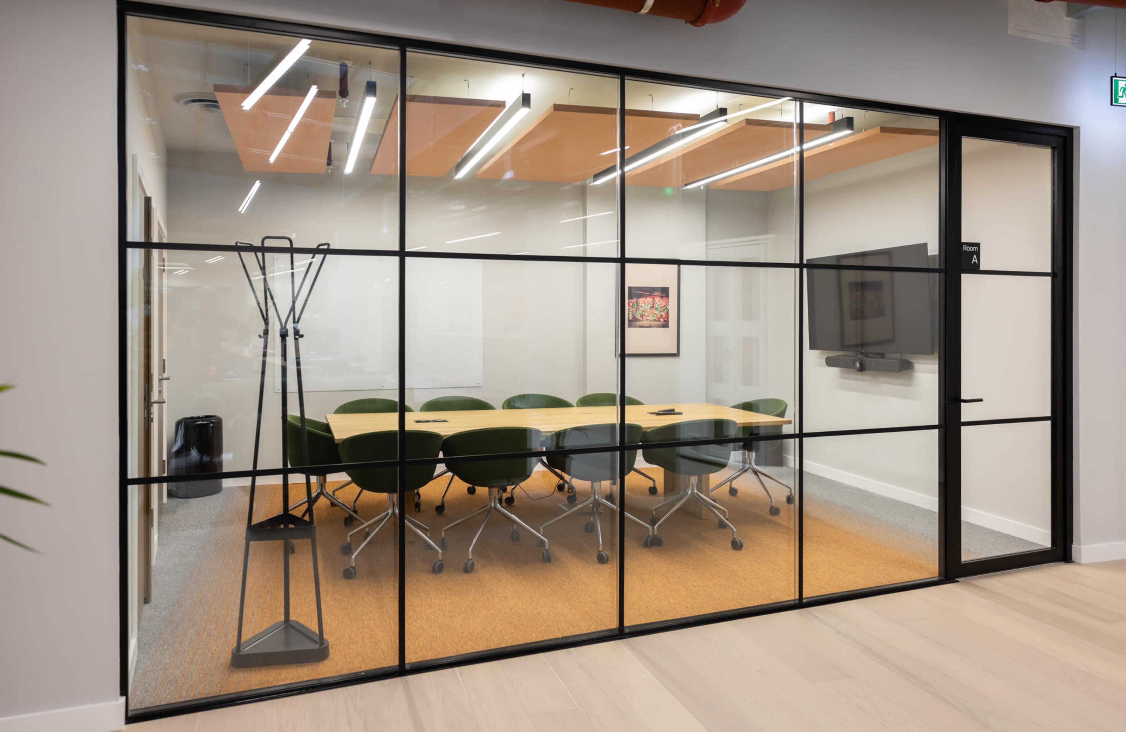 The image shows a modern conference room with a large table surrounded by green chairs, enclosed by glass walls.