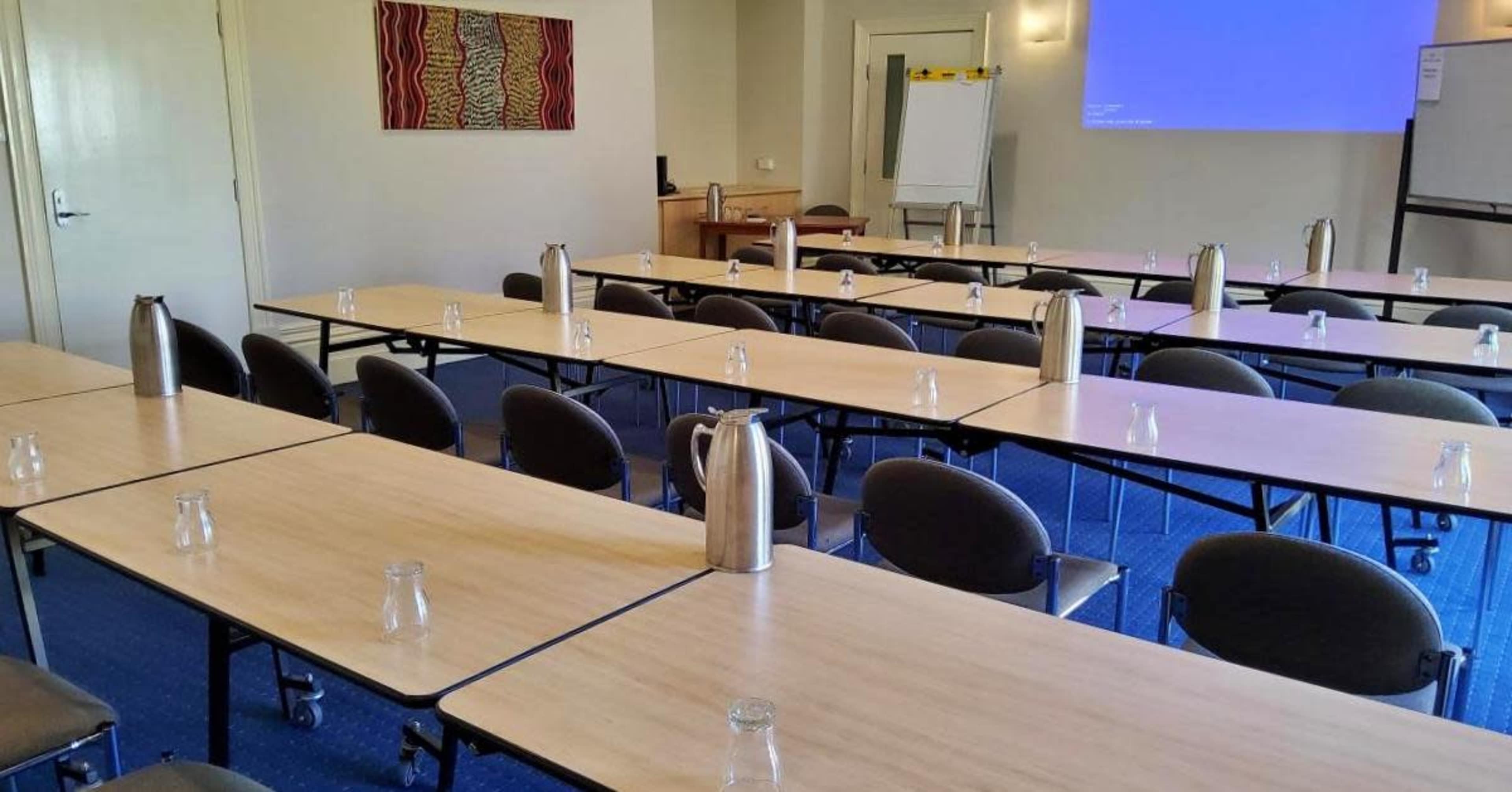 The image shows a conference room set up with multiple tables arranged in a U-shape, each equipped with water pitchers and small glasses.