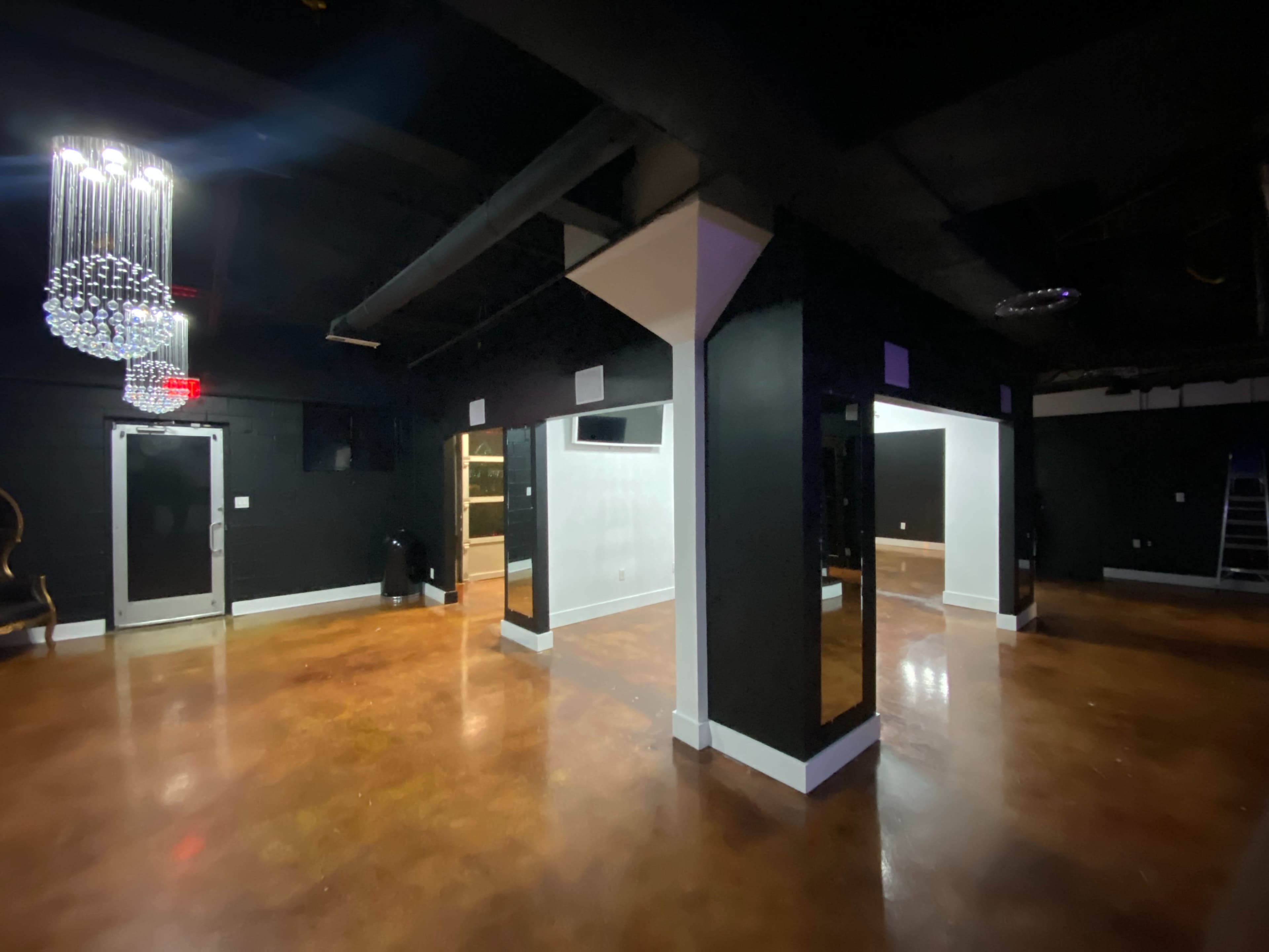 The image shows an empty room with black walls, polished concrete floors, and decorative lighting fixtures hanging from the ceiling.