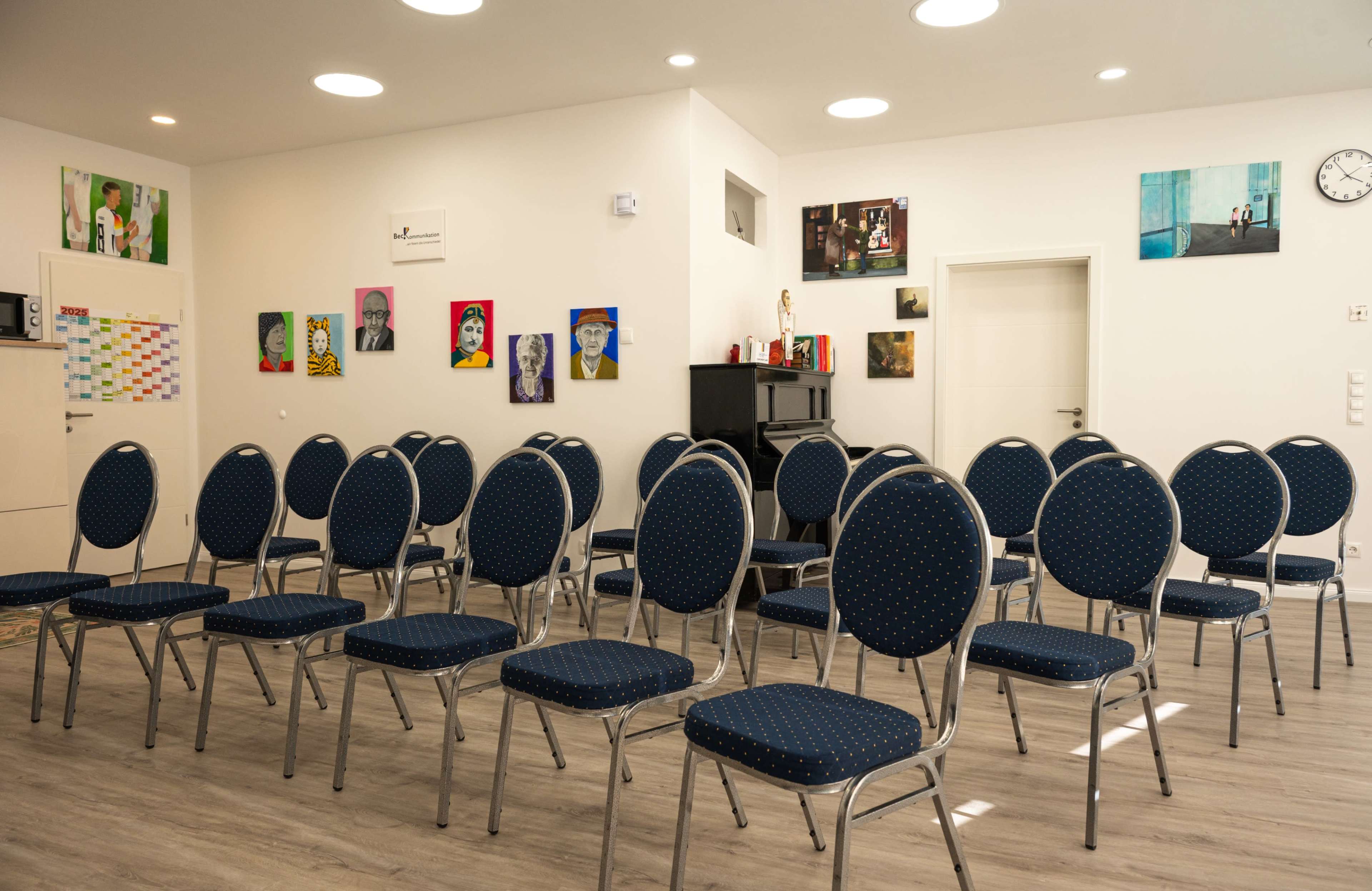 The image shows a room with several metal chairs arranged in rows, decorated with colorful wall art and featuring bright overhead lighting.