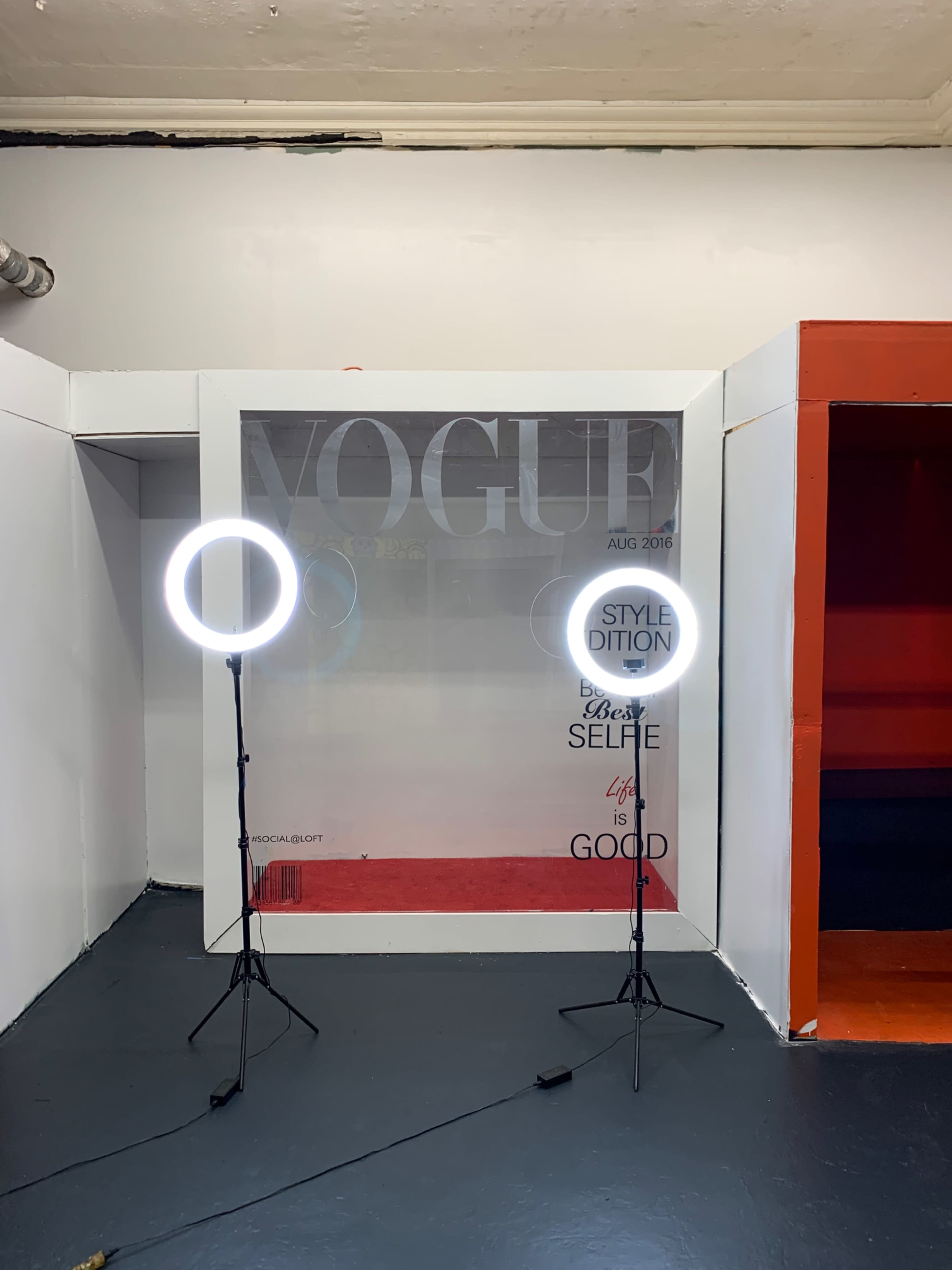 Two ring lights stand on stands in front of a wall featuring a large "VOGUE" sign and graphic text.
