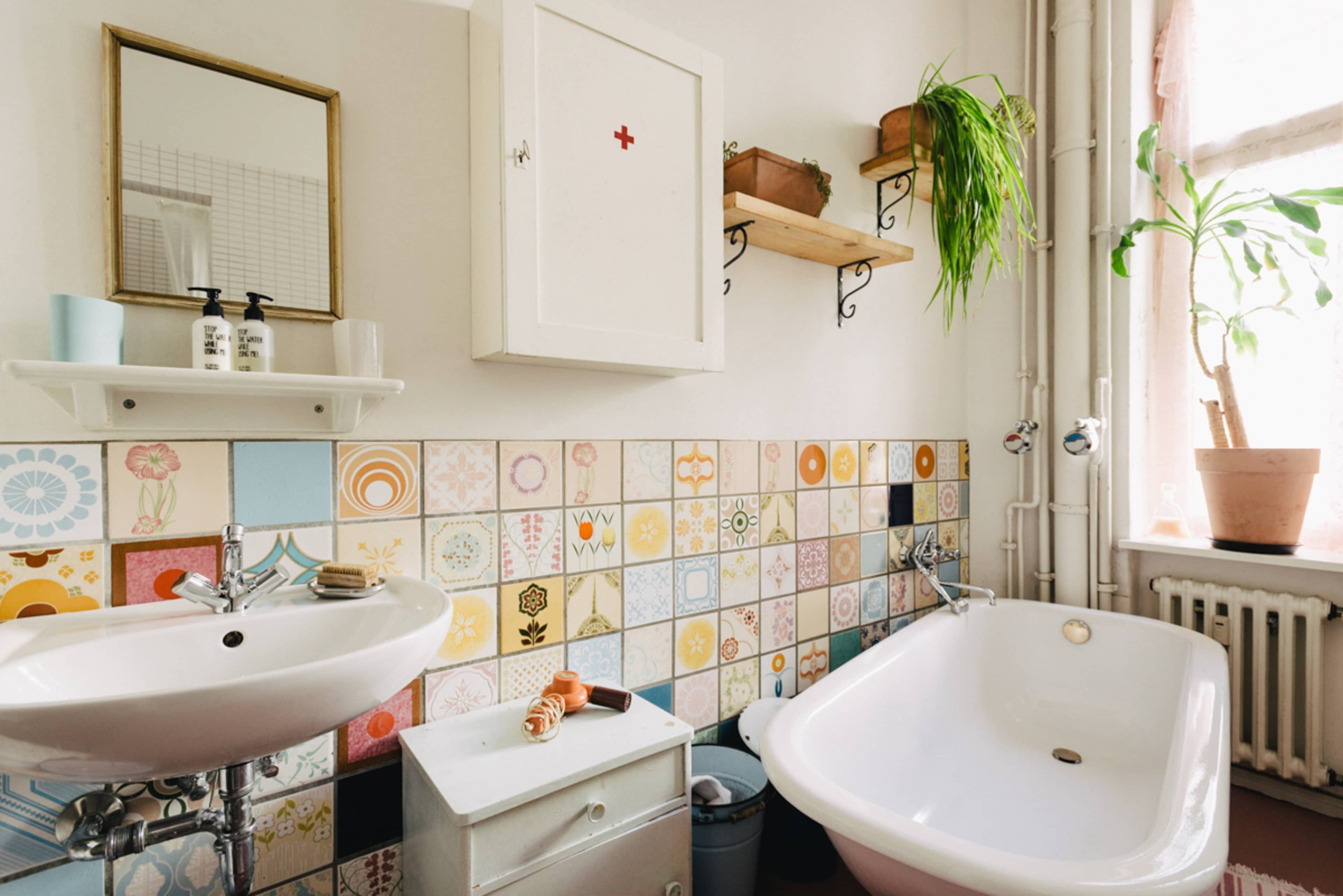 The image shows a bathroom featuring a white bathtub, a sink with toiletries, and a colorful tiled wall with floral patterns.