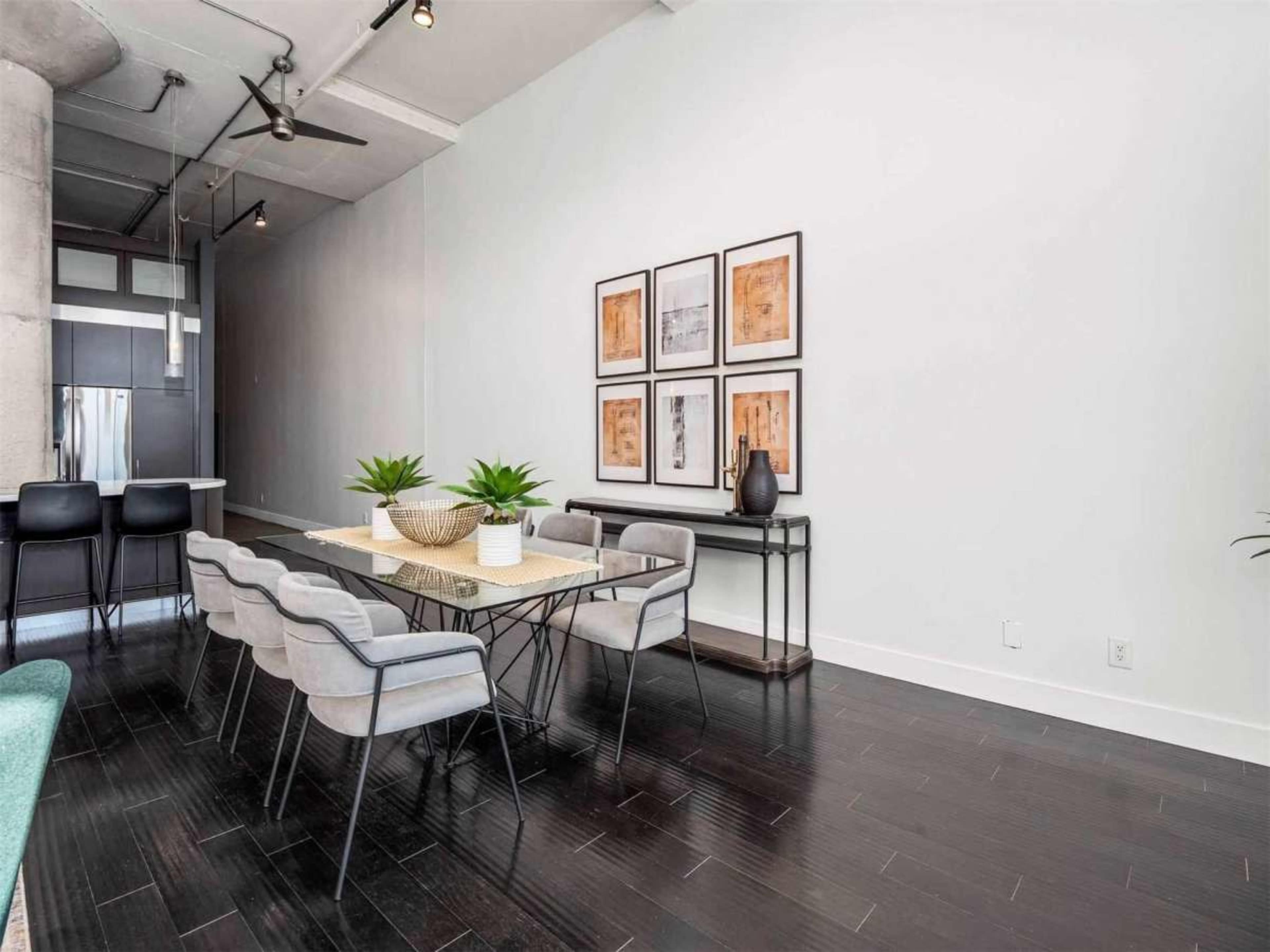 The image shows a modern dining area with a table surrounded by chairs, framed artwork on the wall, and potted plants placed on the table.