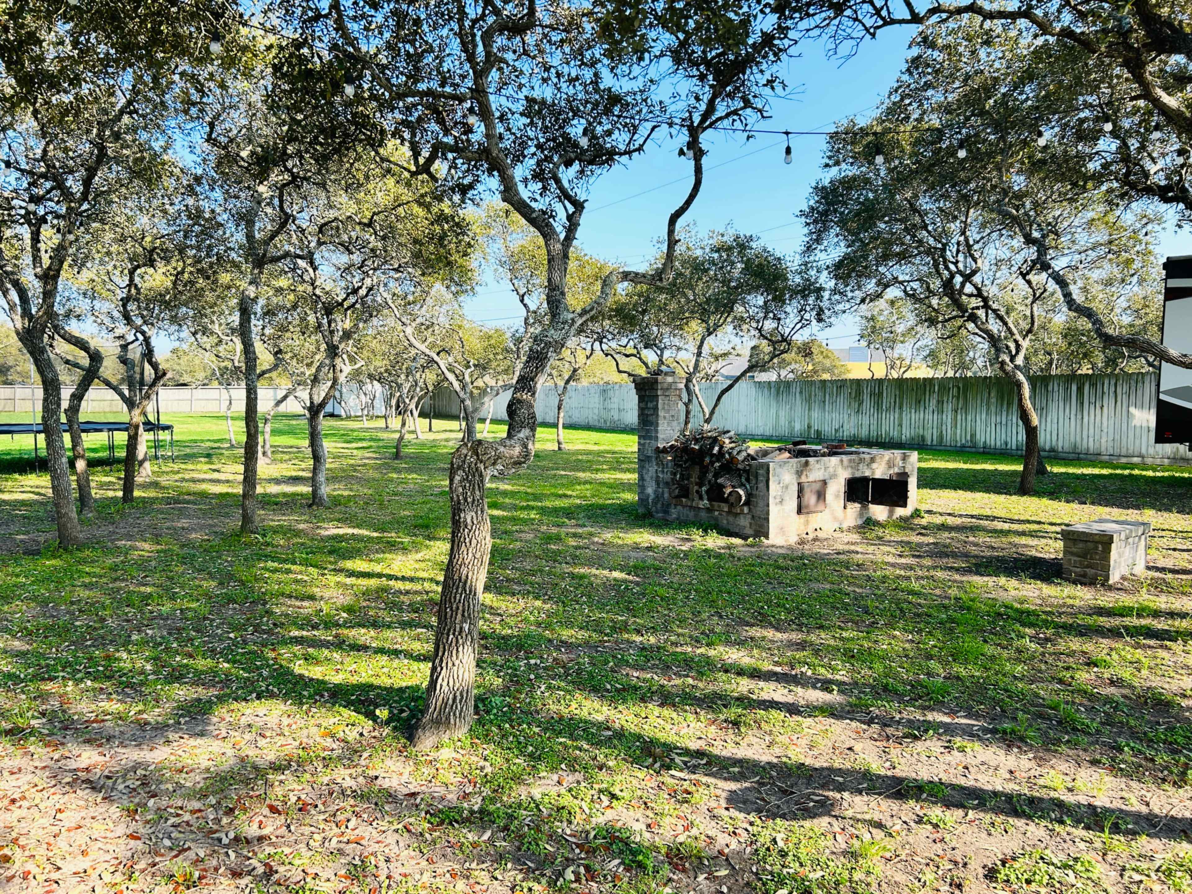 A grassy area surrounded by trees, featuring a stone barbecue grill and a bench.