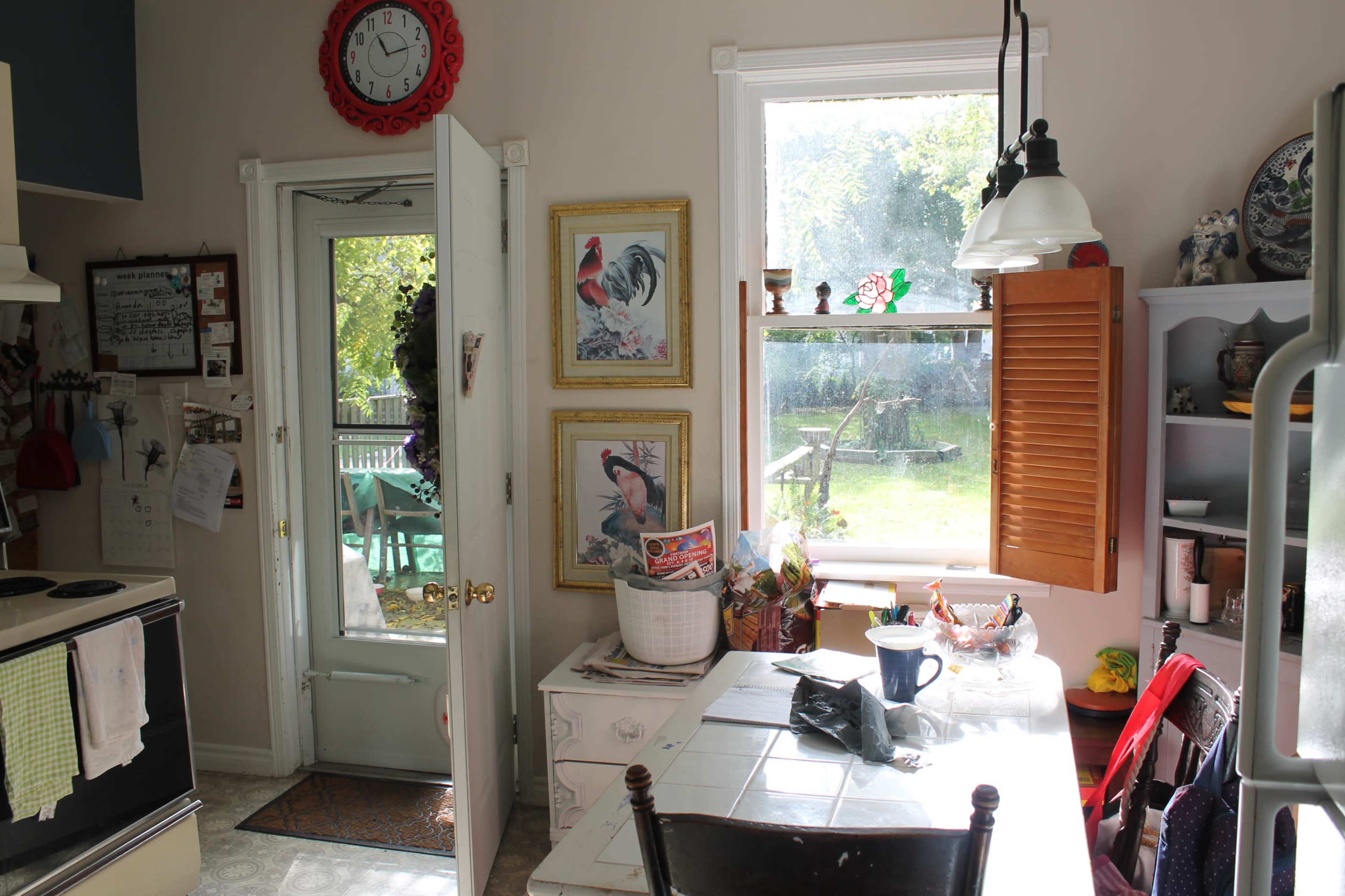 A kitchen with a door leading to an outdoor space, featuring a table, chairs, and framed pictures on the walls, illuminated by natural light.