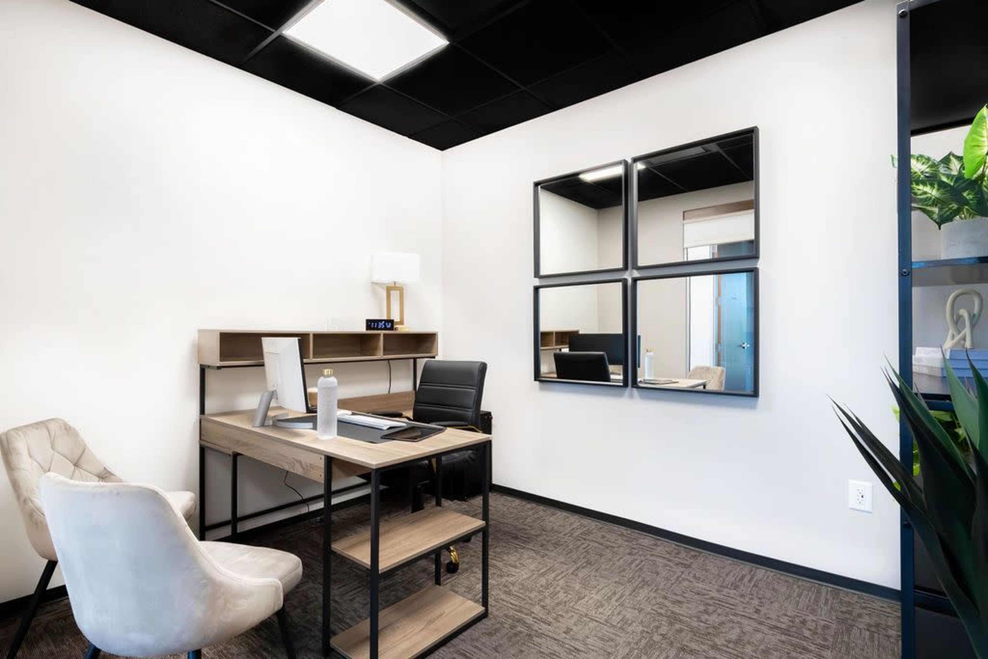 The image shows a small office space with a desk, a chair, and a large set of four mirrors on the wall.