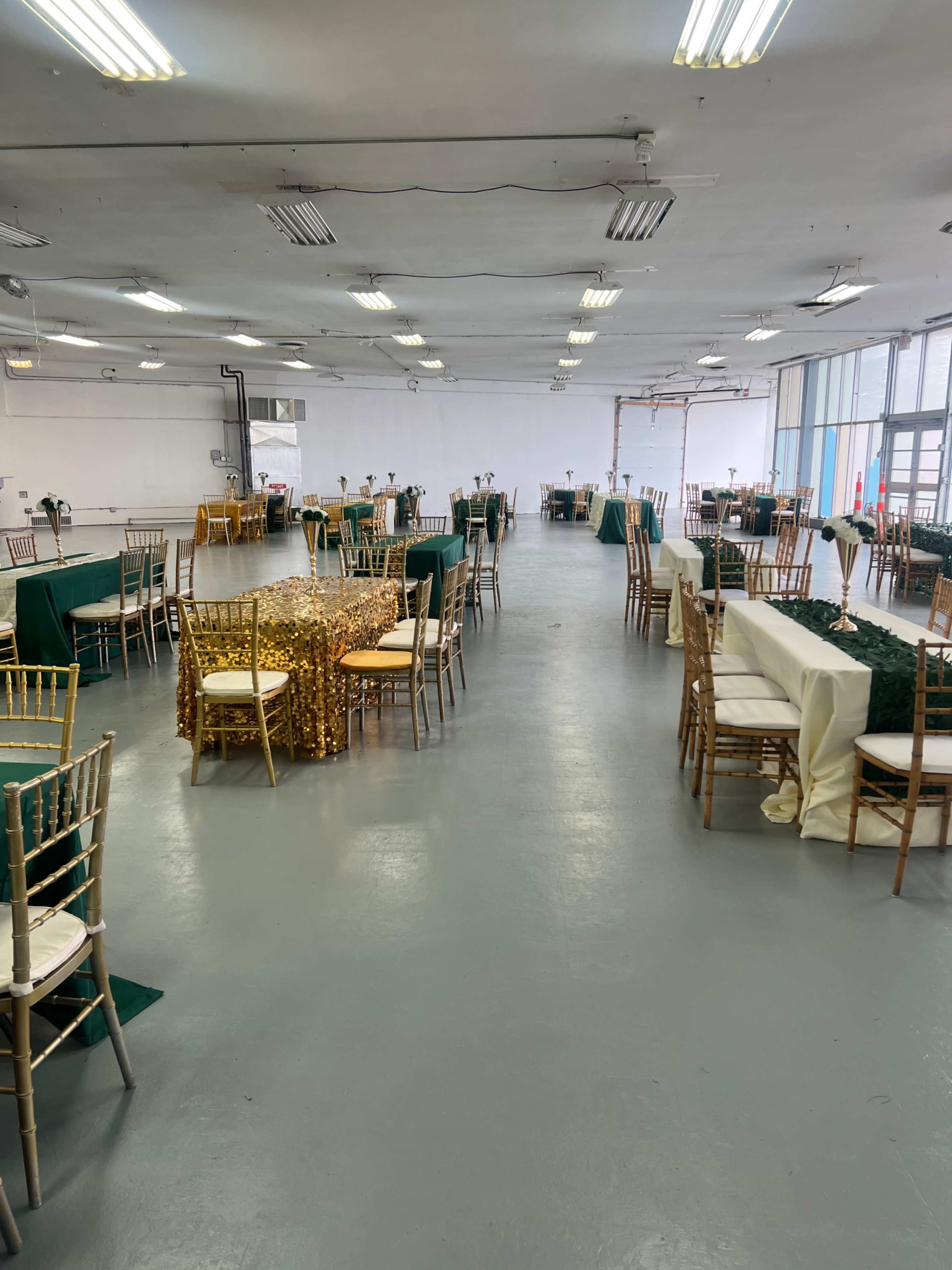 A large, empty indoor space set up with gold and green tablecloths and chairs arranged for an event.