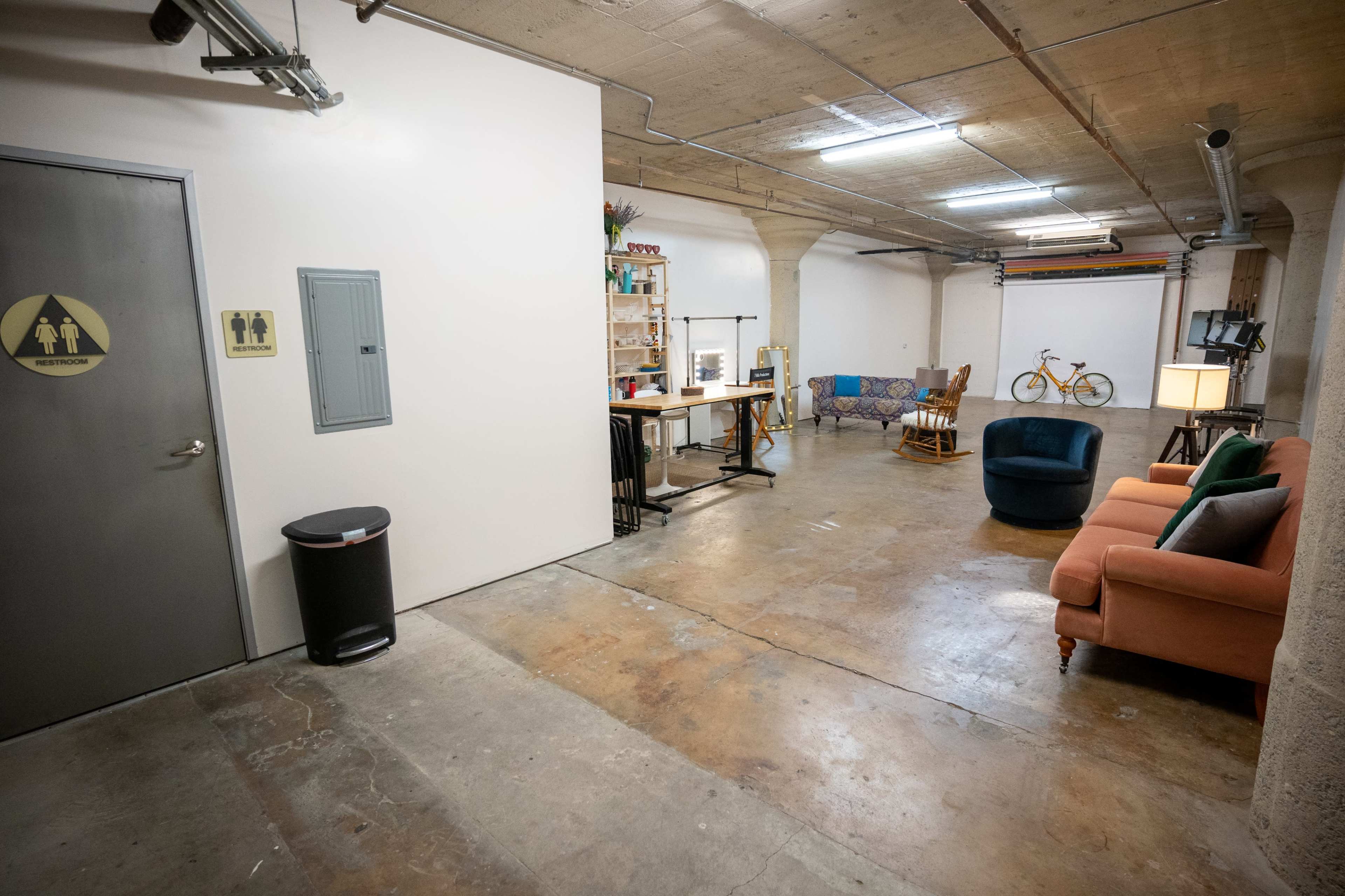 An open workspace with a seating area, a desk with office supplies, and a restroom door on the left.