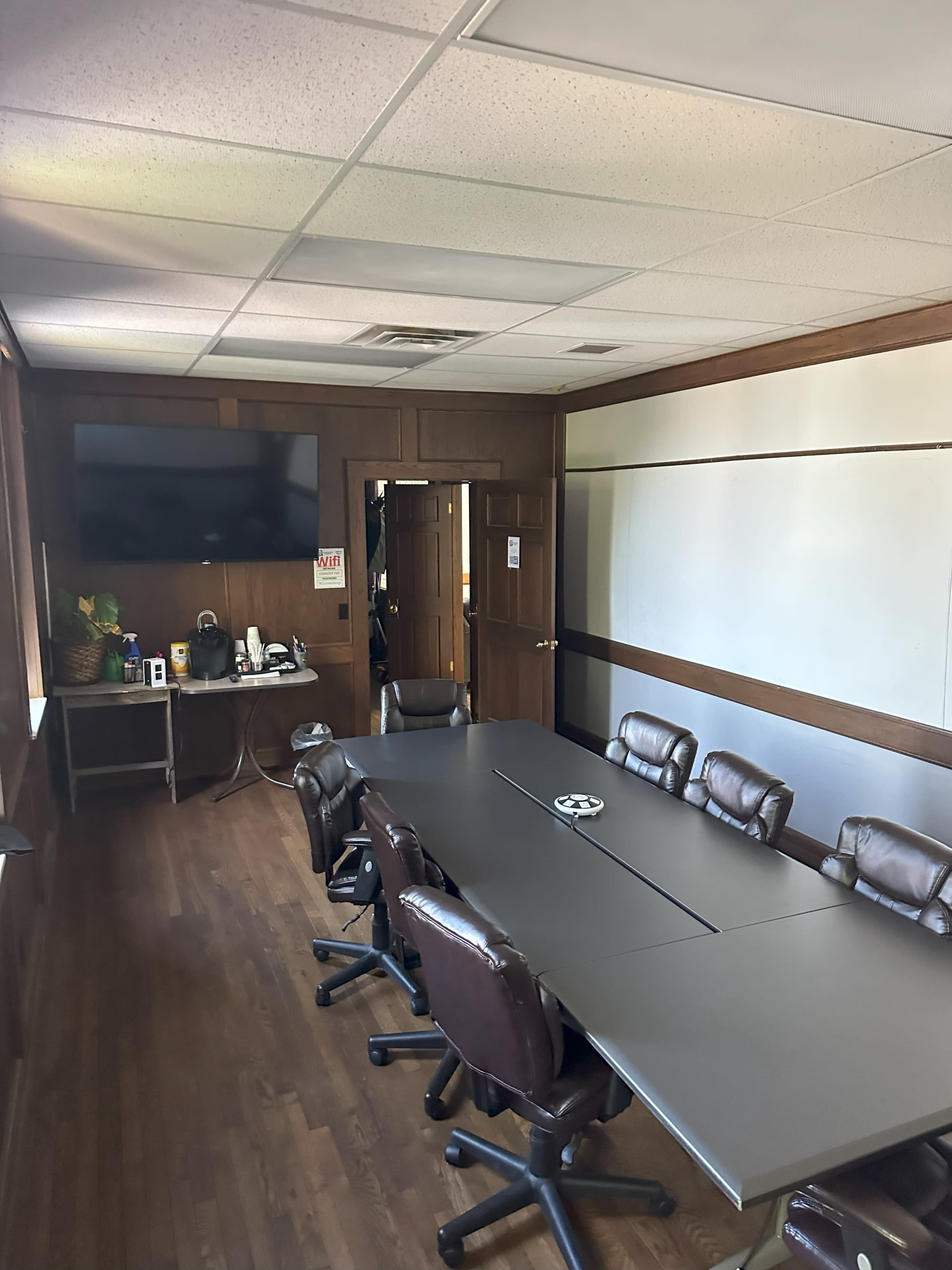 A conference room with a long table, several chairs, a wall-mounted TV, and a door leading outside.