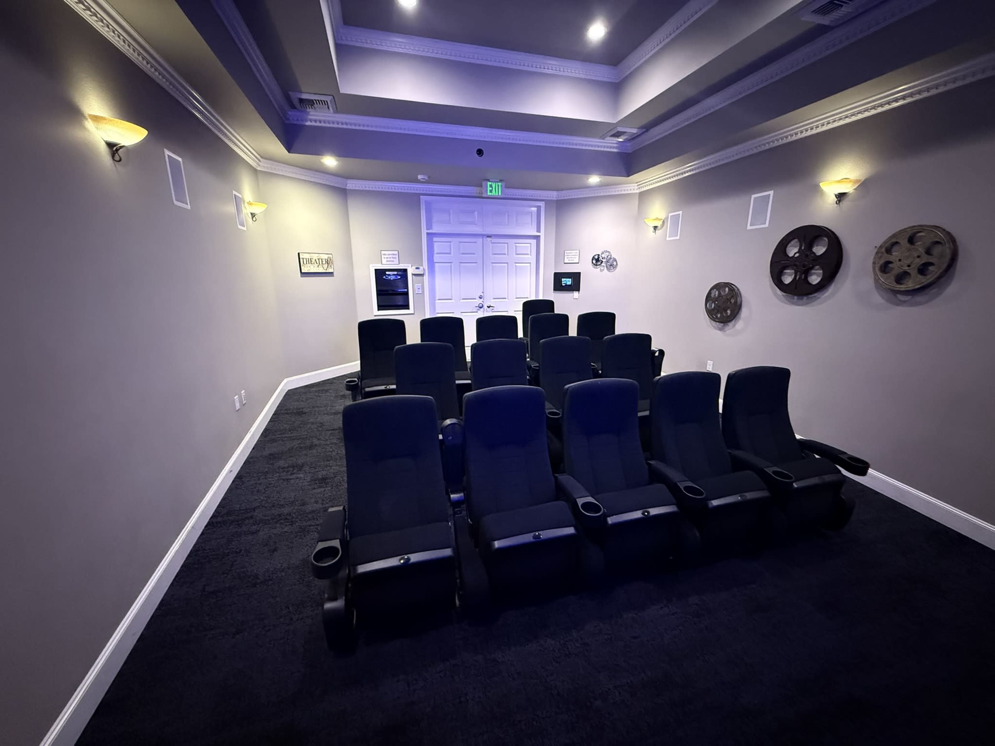 The image shows a small home theater room with ten black reclining chairs arranged in rows, and film reels displayed on the walls.