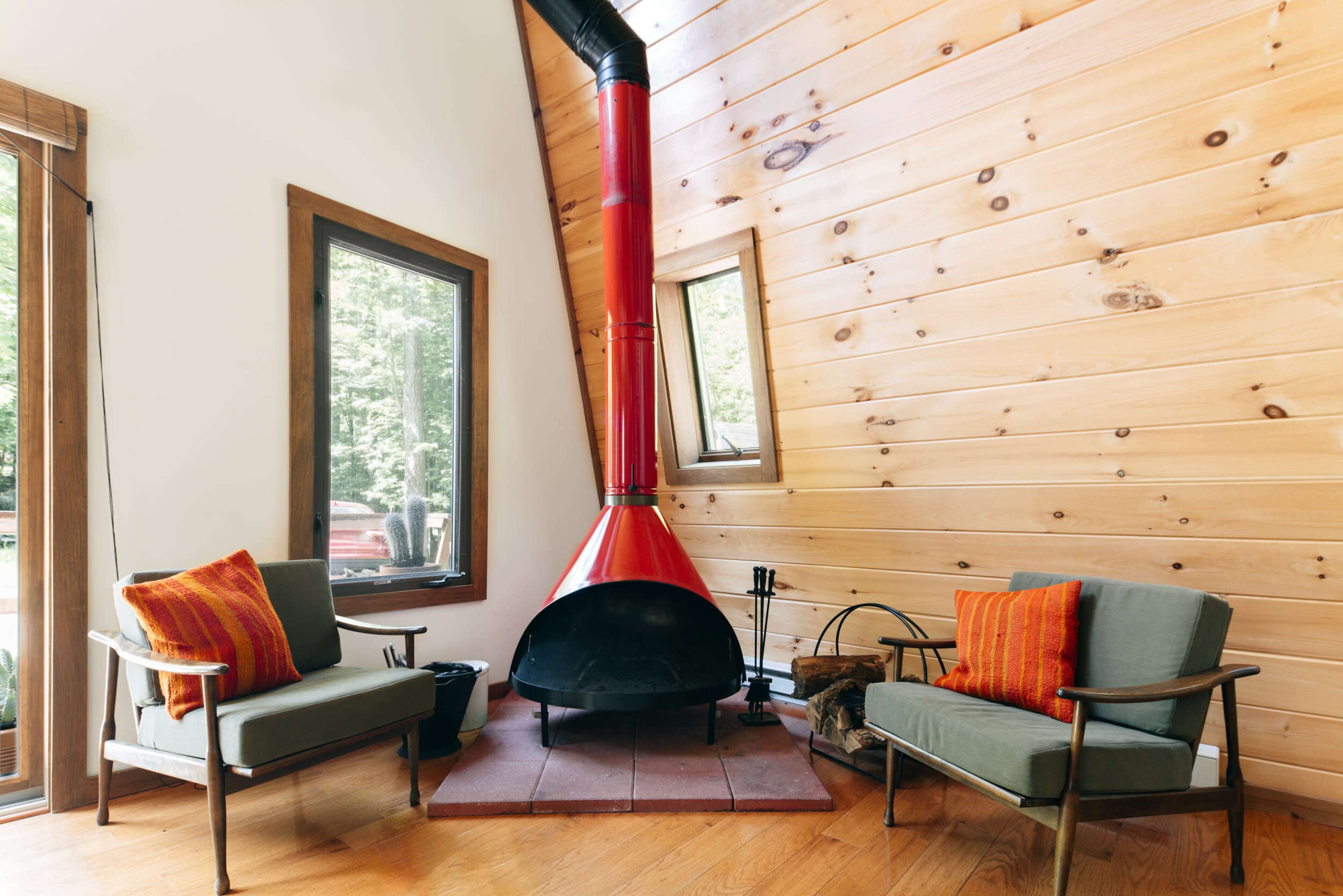 A cozy living space with a red fireplace, two green chairs, and wooden walls.
