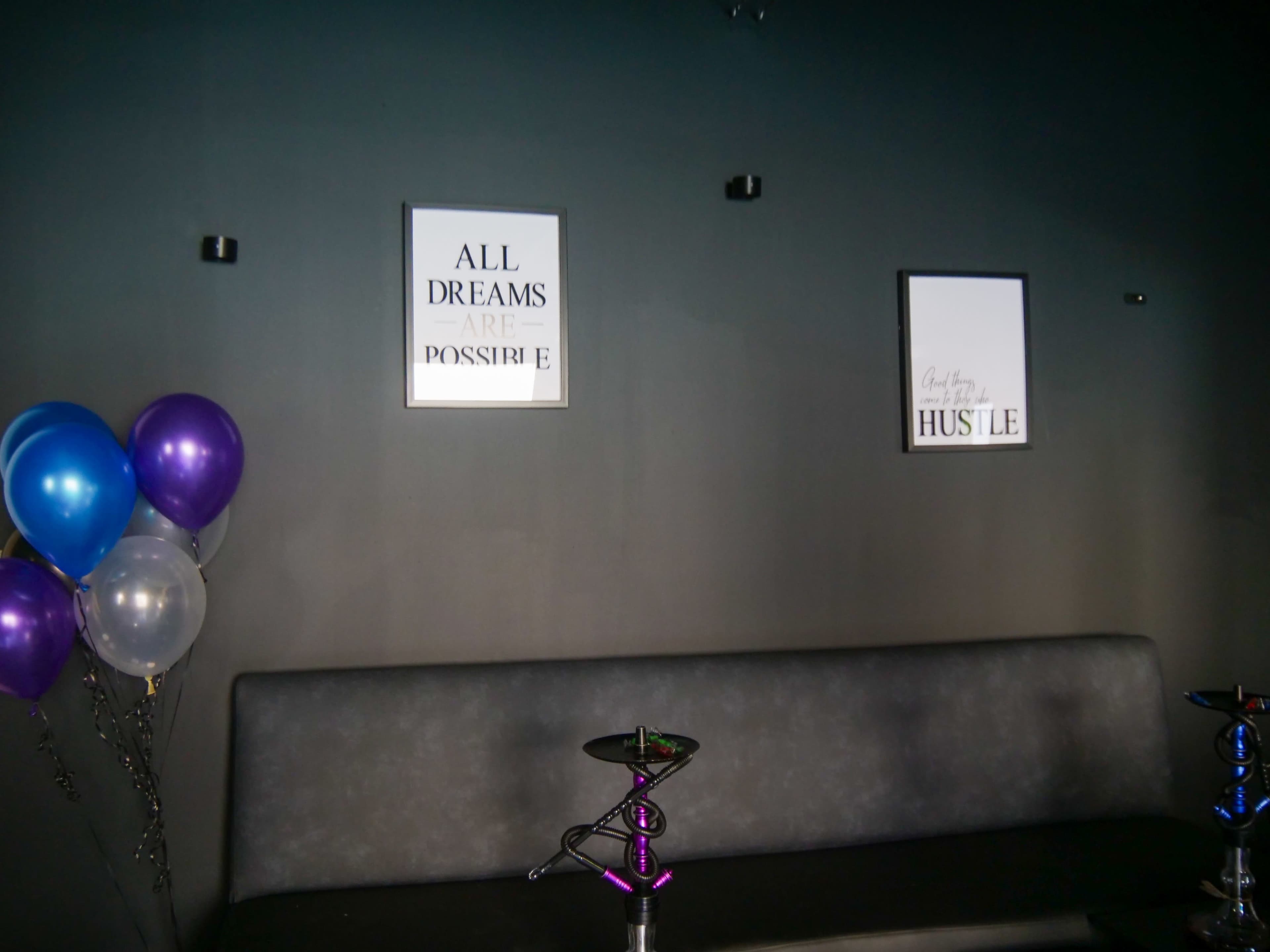 A dark wall with two framed quotes and a gray sofa, alongside three balloons in purple and white.