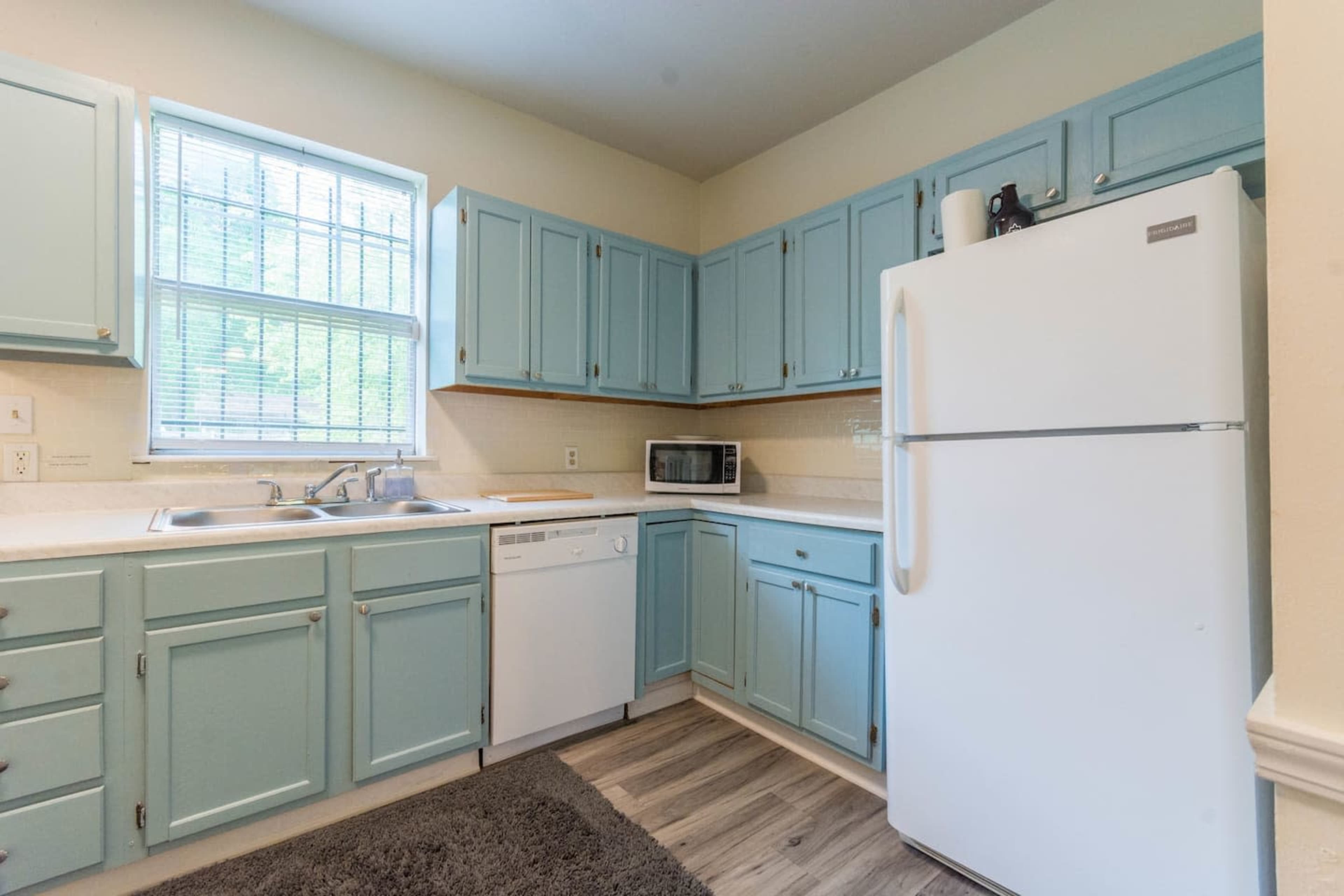 A kitchen with light blue cabinets, a white refrigerator, a sink, a dishwasher, and a microwave on the counter.