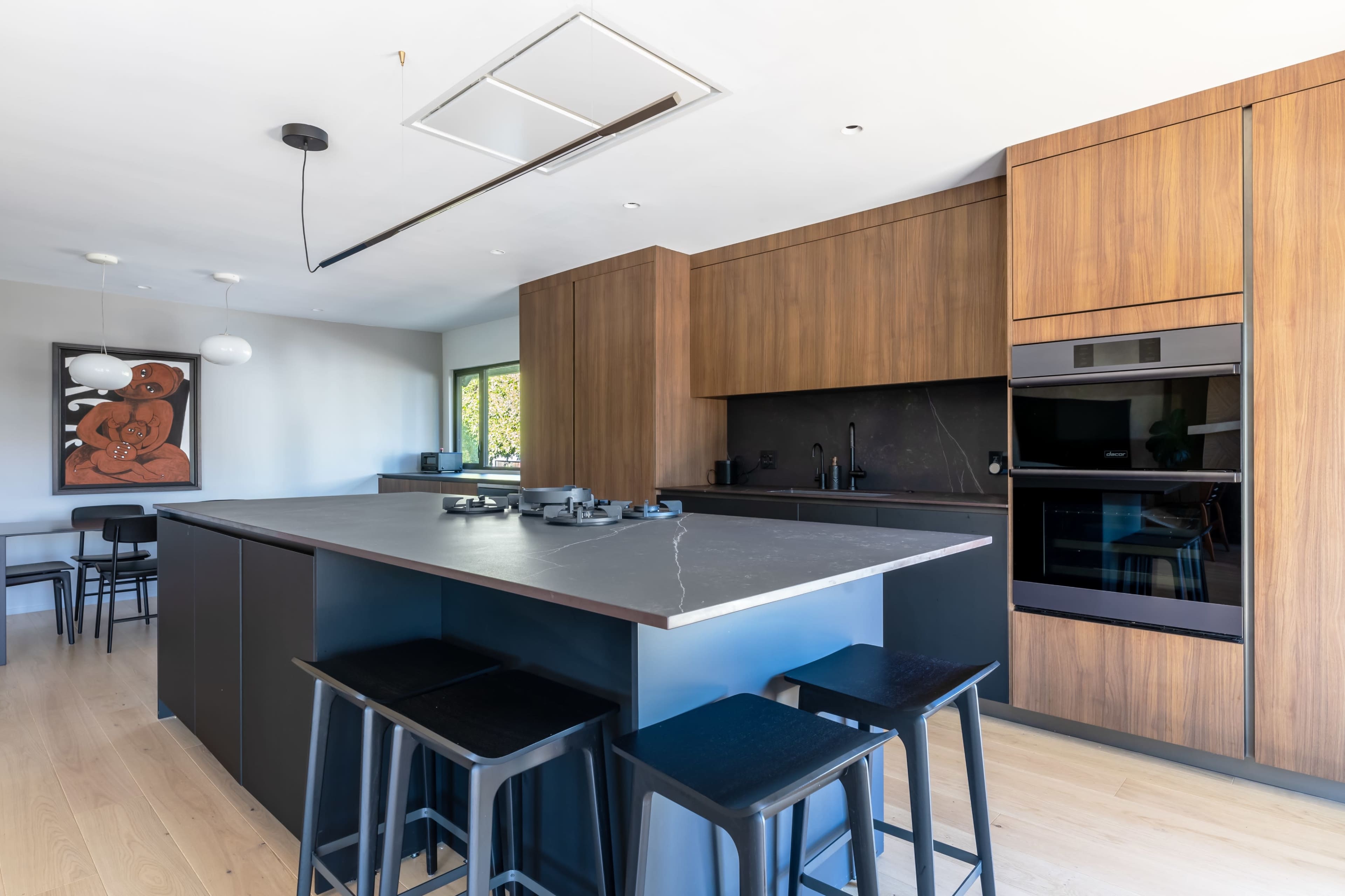 A modern kitchen features dark wood cabinetry, a large island with black stools, and a sleek gray countertop.