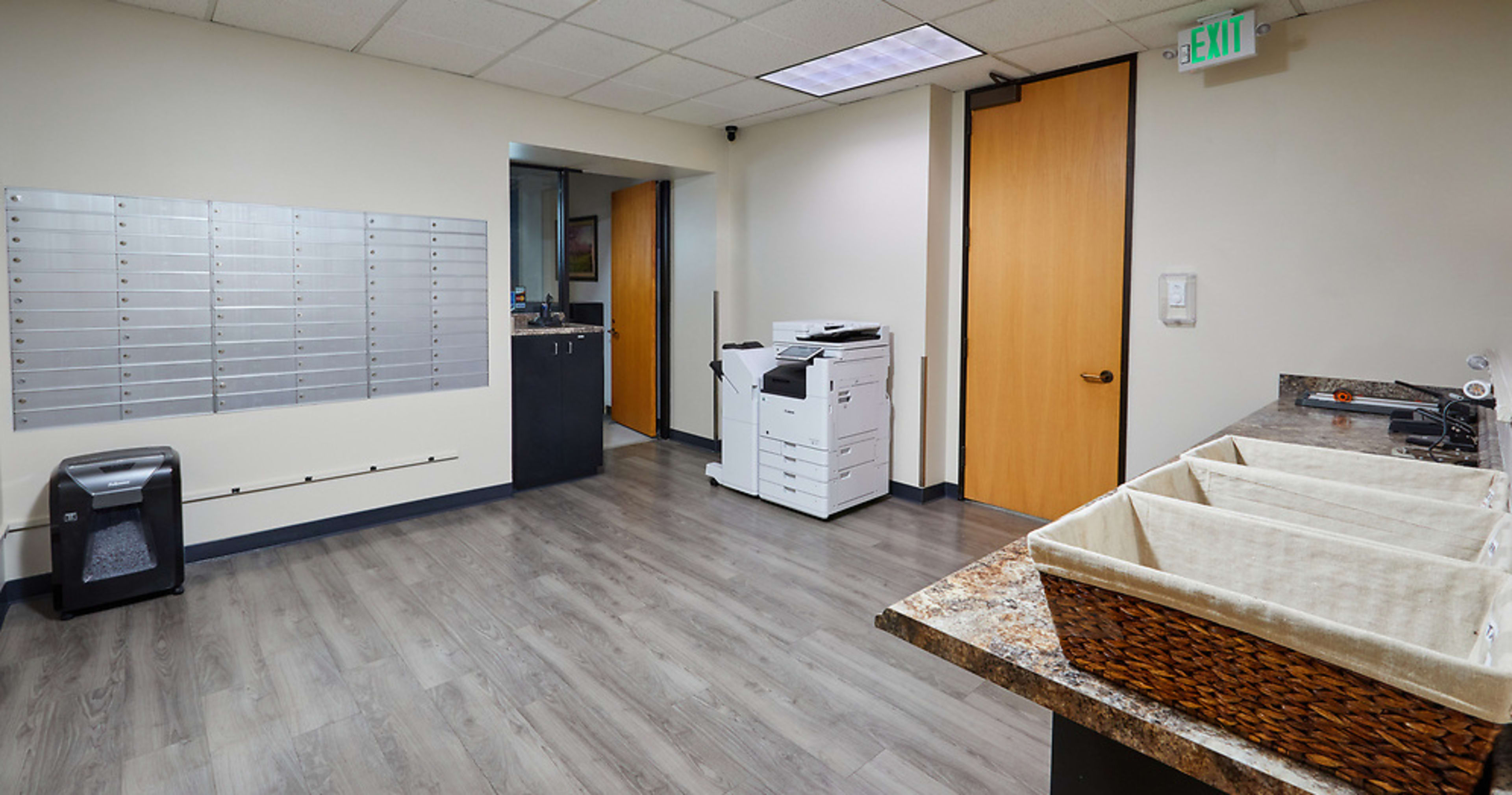 A mailroom with wall-mounted mailboxes on the left, a copier station in the center, and a countertop area with storage bins on the right.