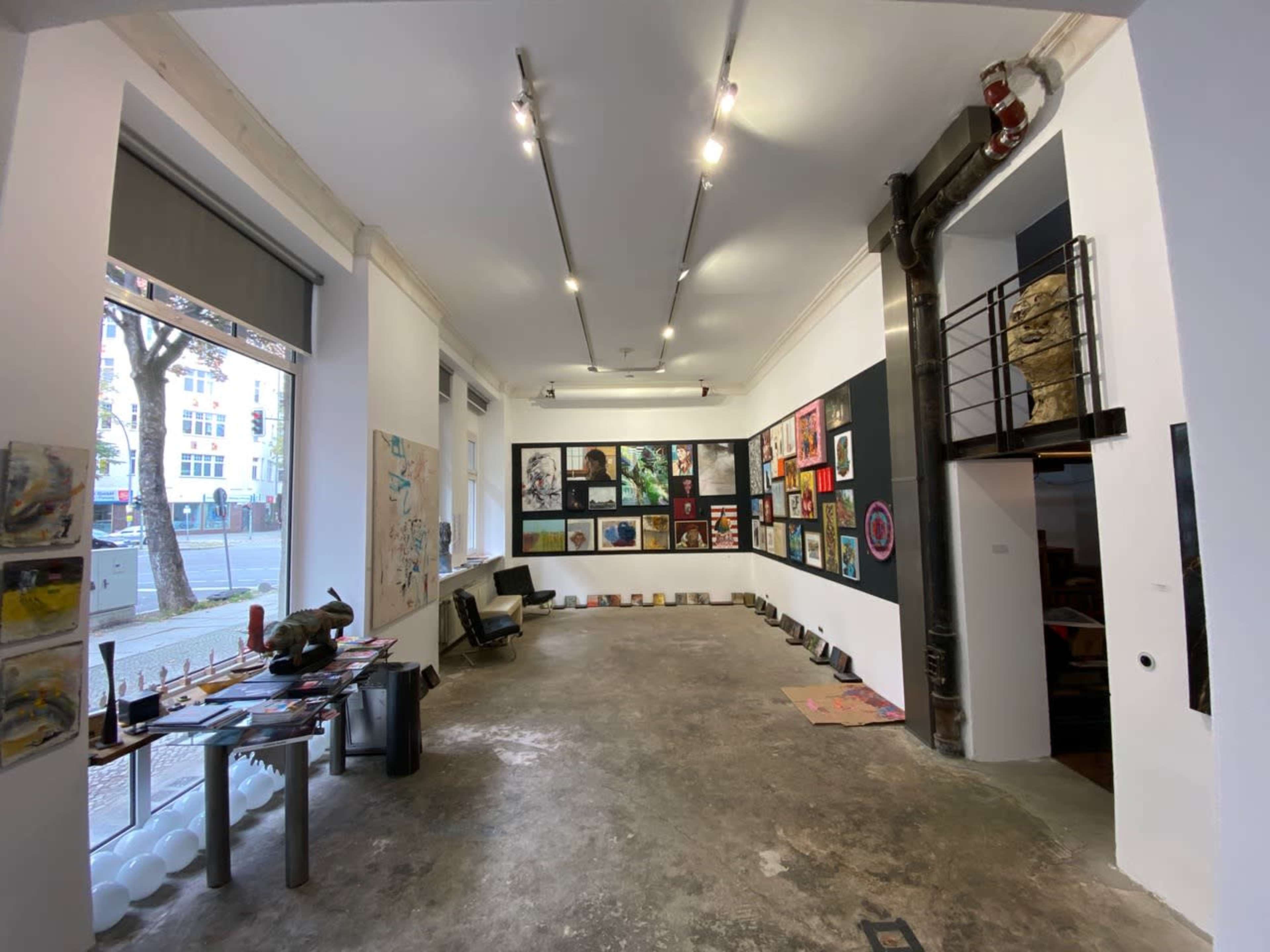 A contemporary art gallery featuring a variety of artworks displayed on the walls and sculptures arranged around a concrete floor.