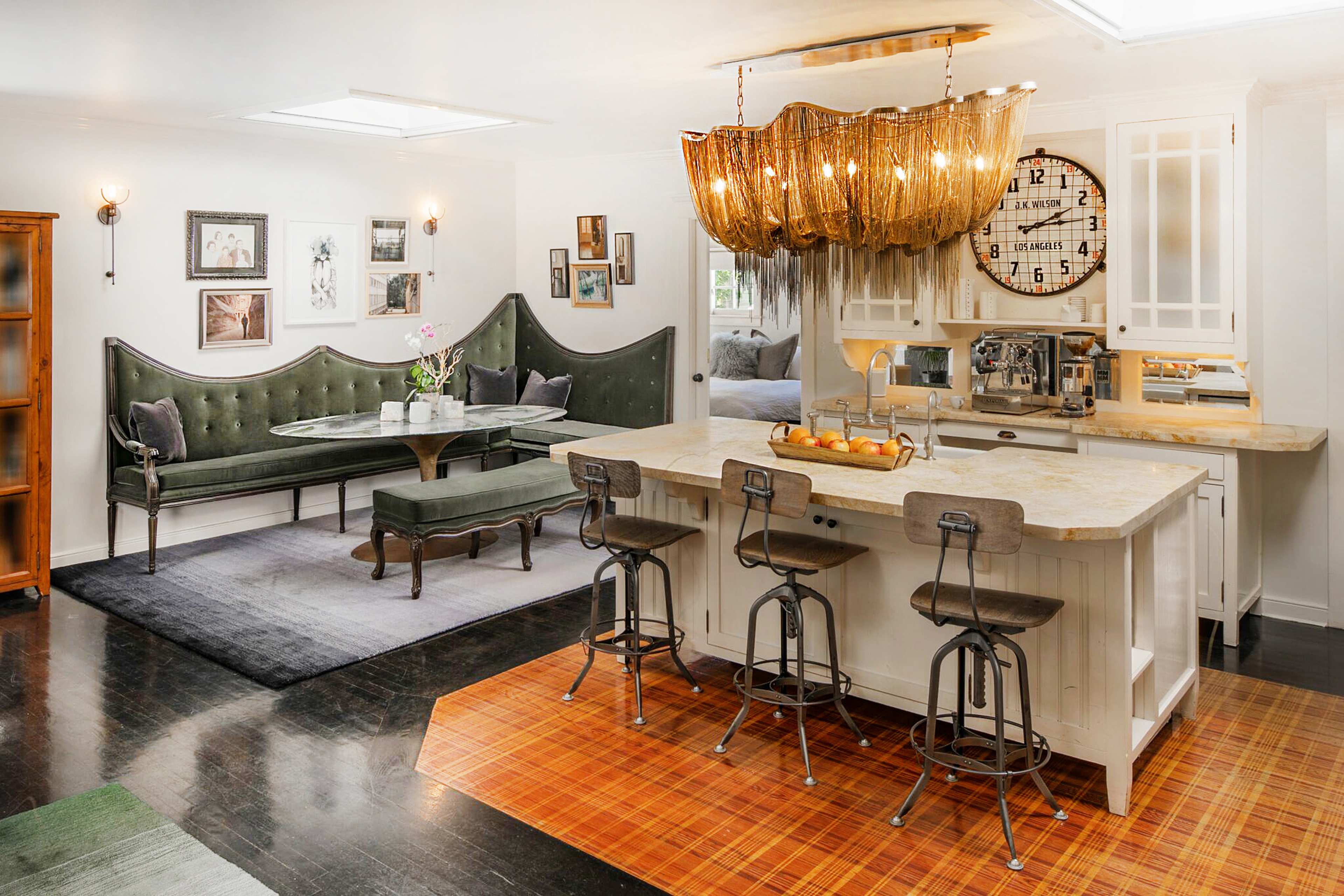 A modern kitchen and living area featuring a green upholstered bench, a wooden table with chairs, and a large, woven pendant light above the kitchen island.