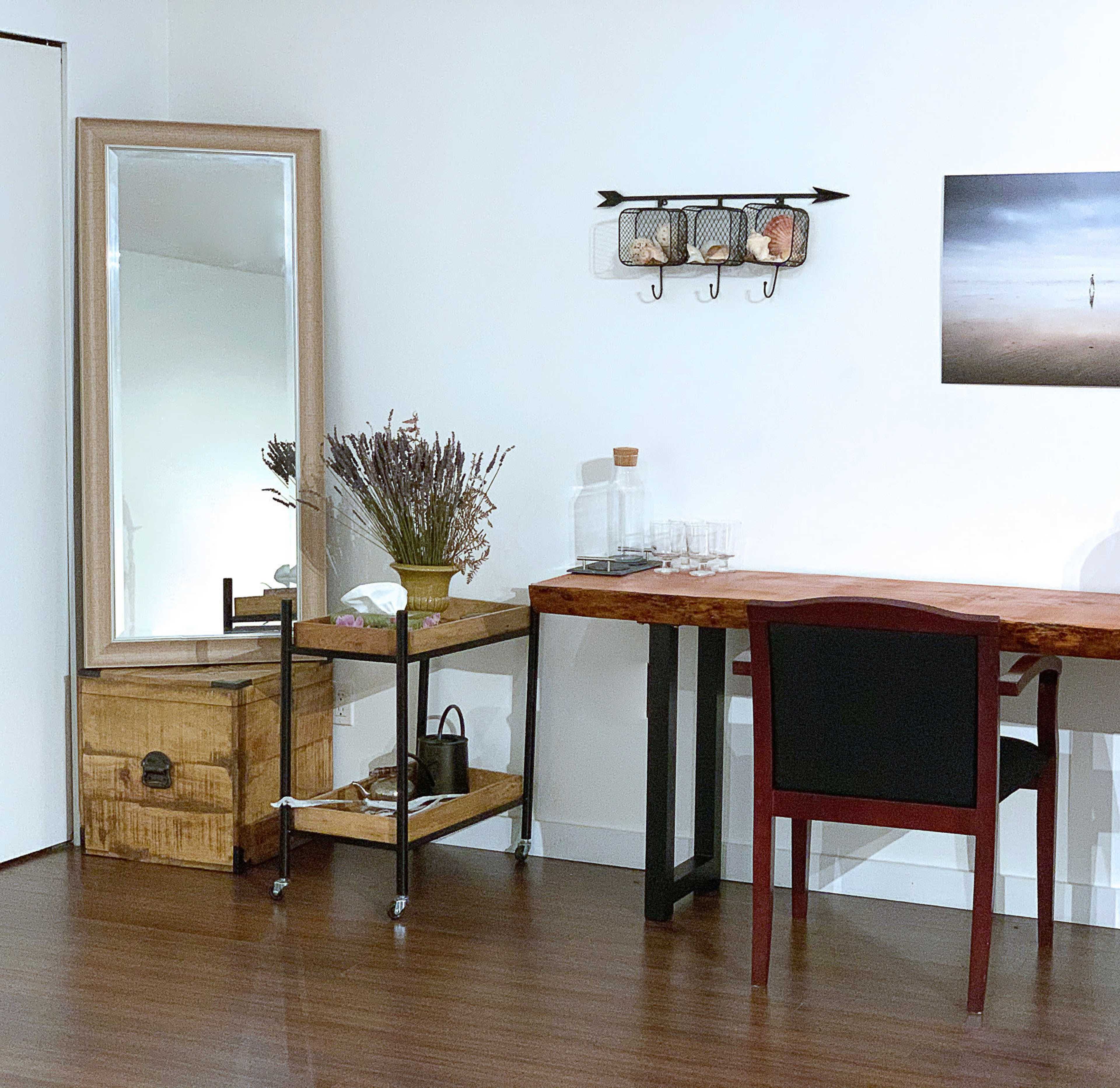 A modern room featuring a mirror, a wooden table, a cart with decorative items, and a wall-mounted rack.