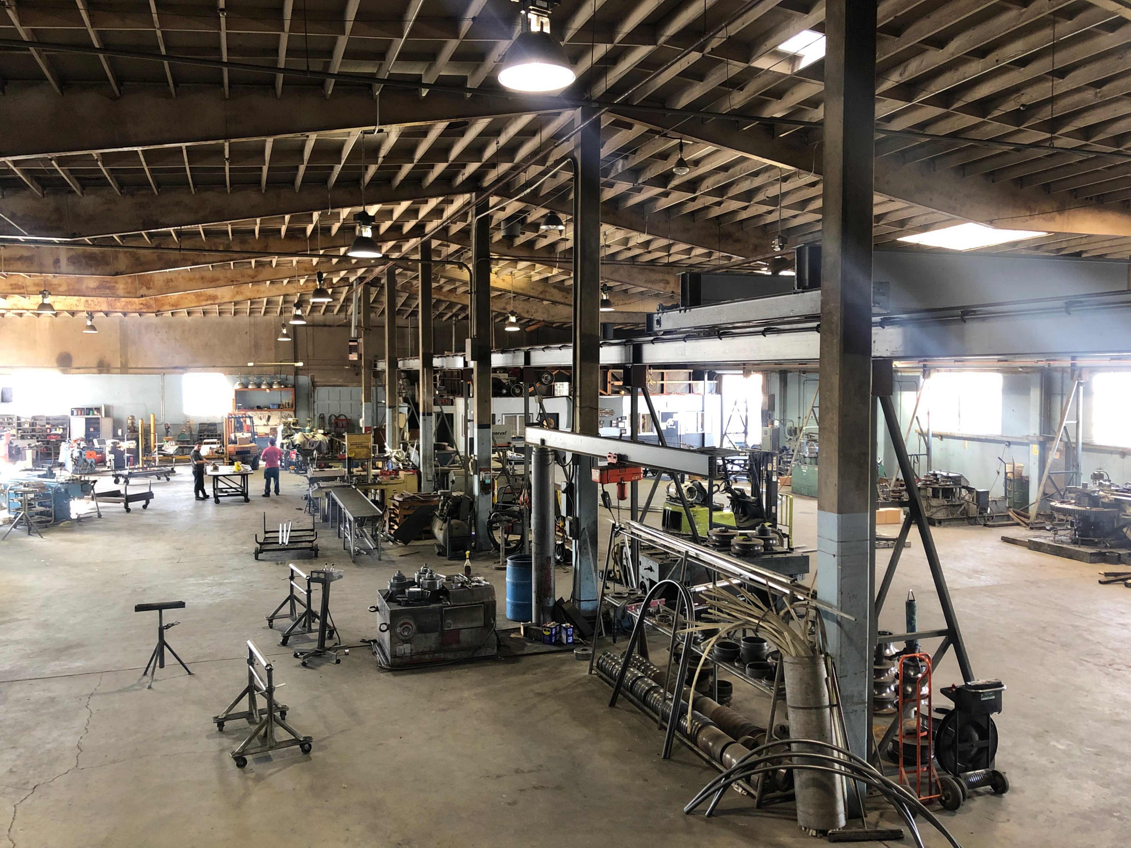 The image shows a large industrial workshop with various machinery, tools, and workstations organized throughout the space.