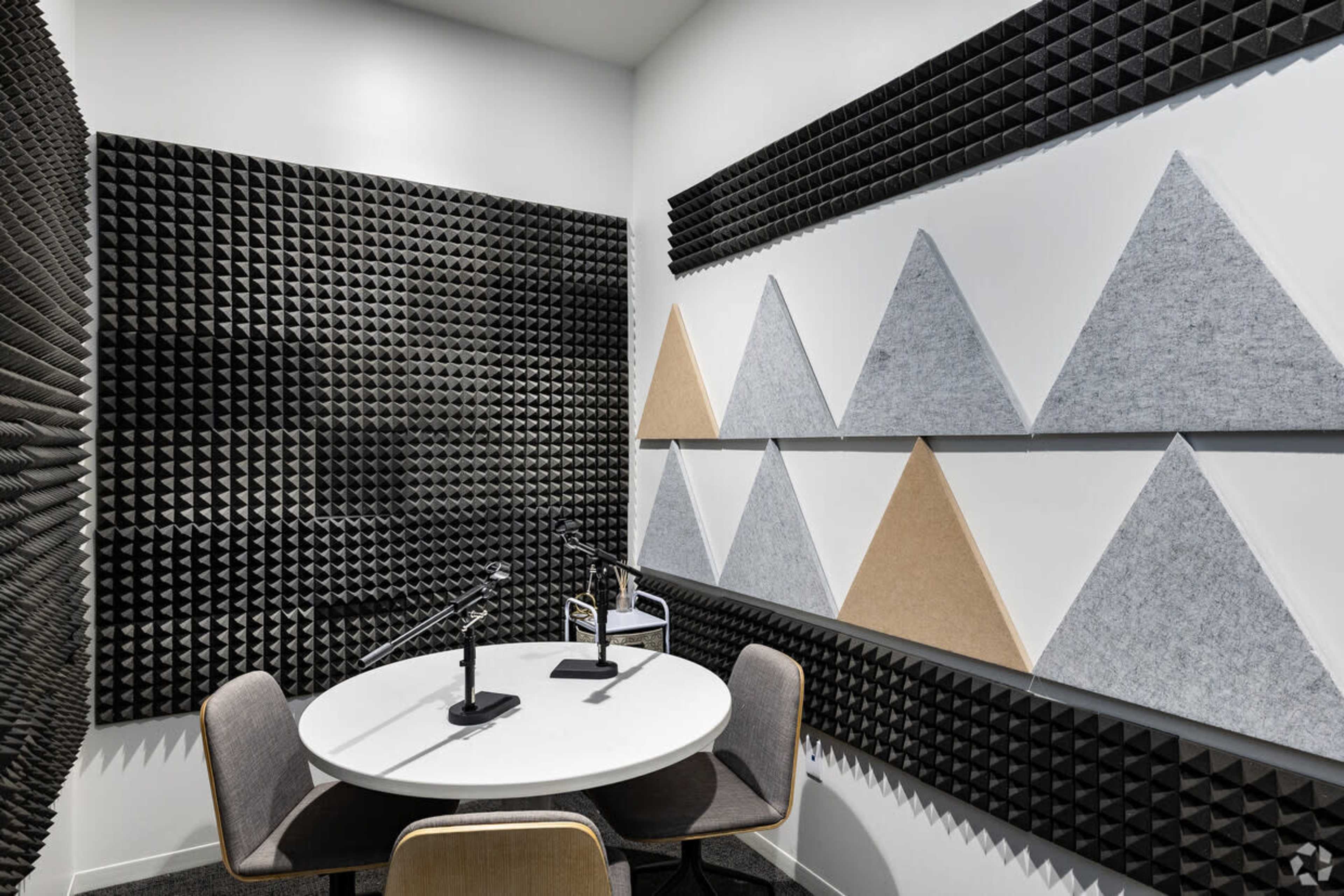 The image shows a small soundproof room equipped with a round table and two microphones, featuring textured acoustic panels on the walls.