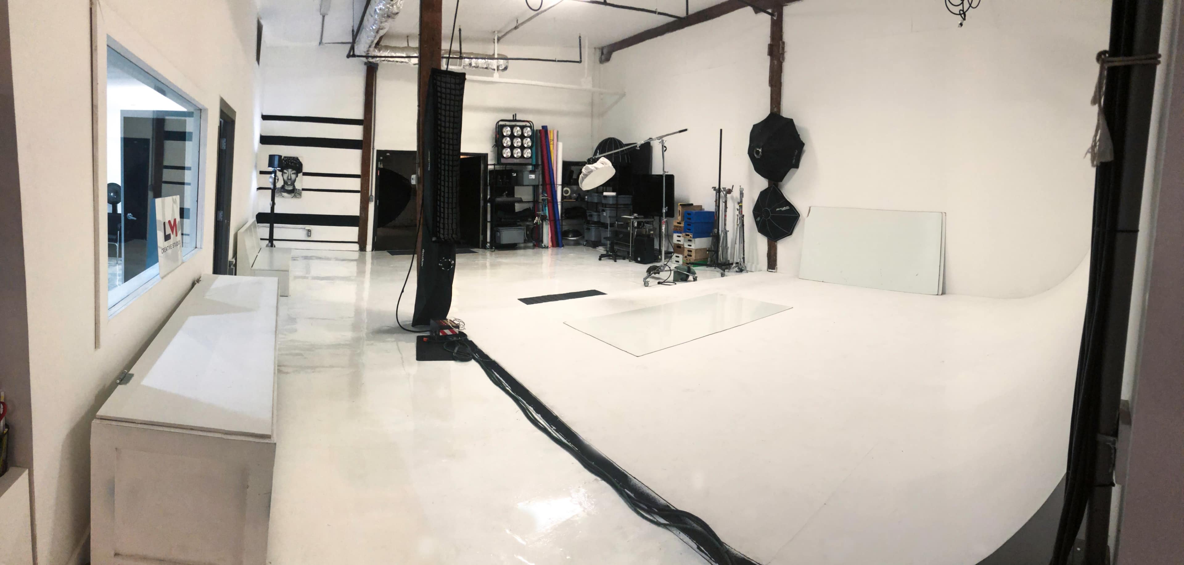 A spacious photography studio with a white floor, backdrop, and various lighting equipment set against bare walls.